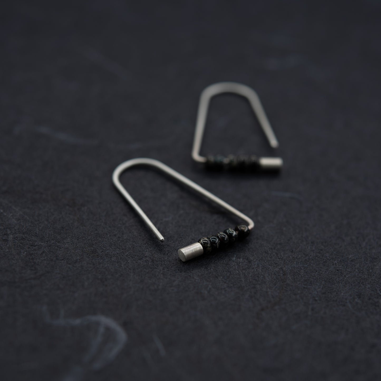 Boucles triangulaires en argent et perles Miyuki, disposées à plat sur fond foncé.