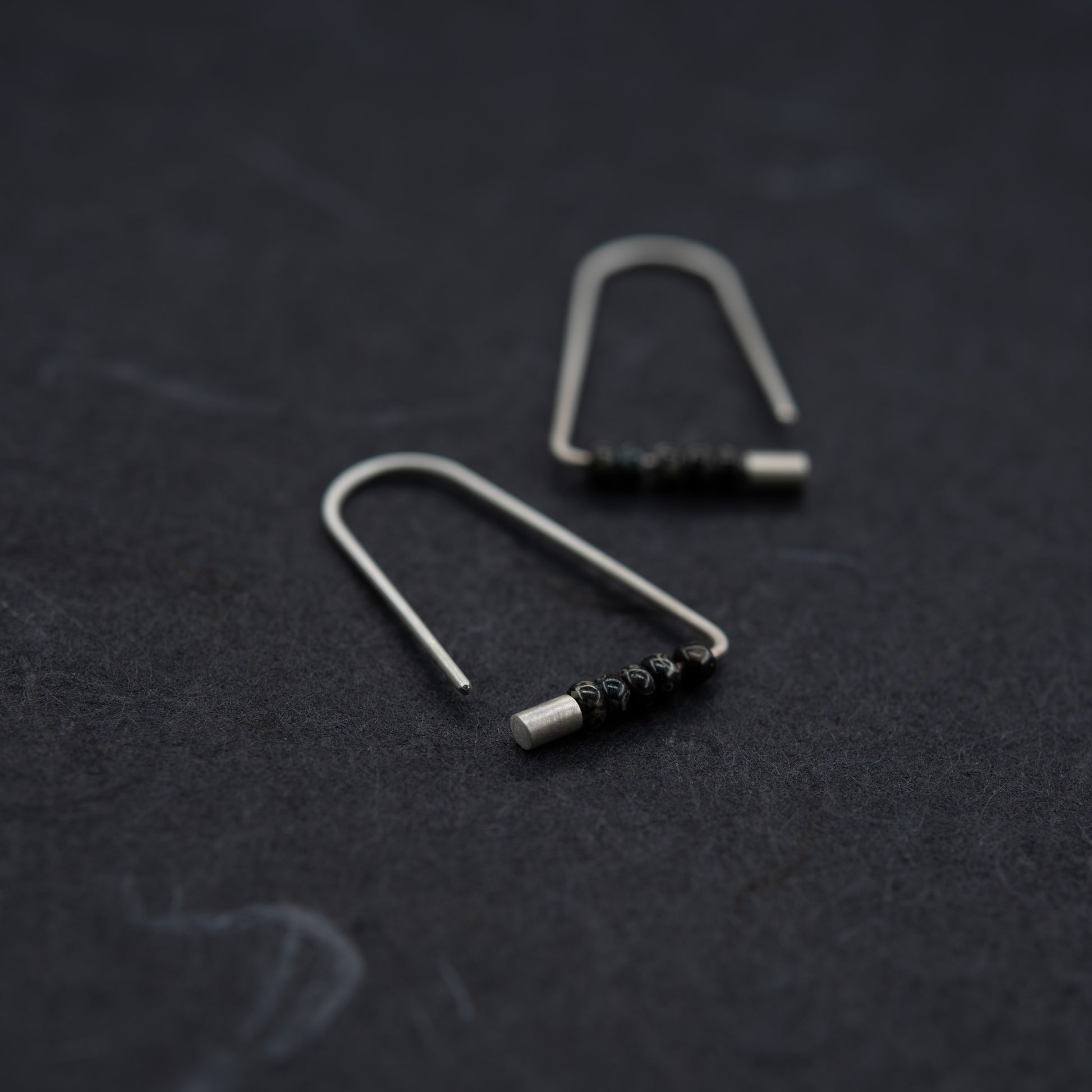 Boucles triangulaires en argent et perles Miyuki, disposées à plat sur fond foncé.