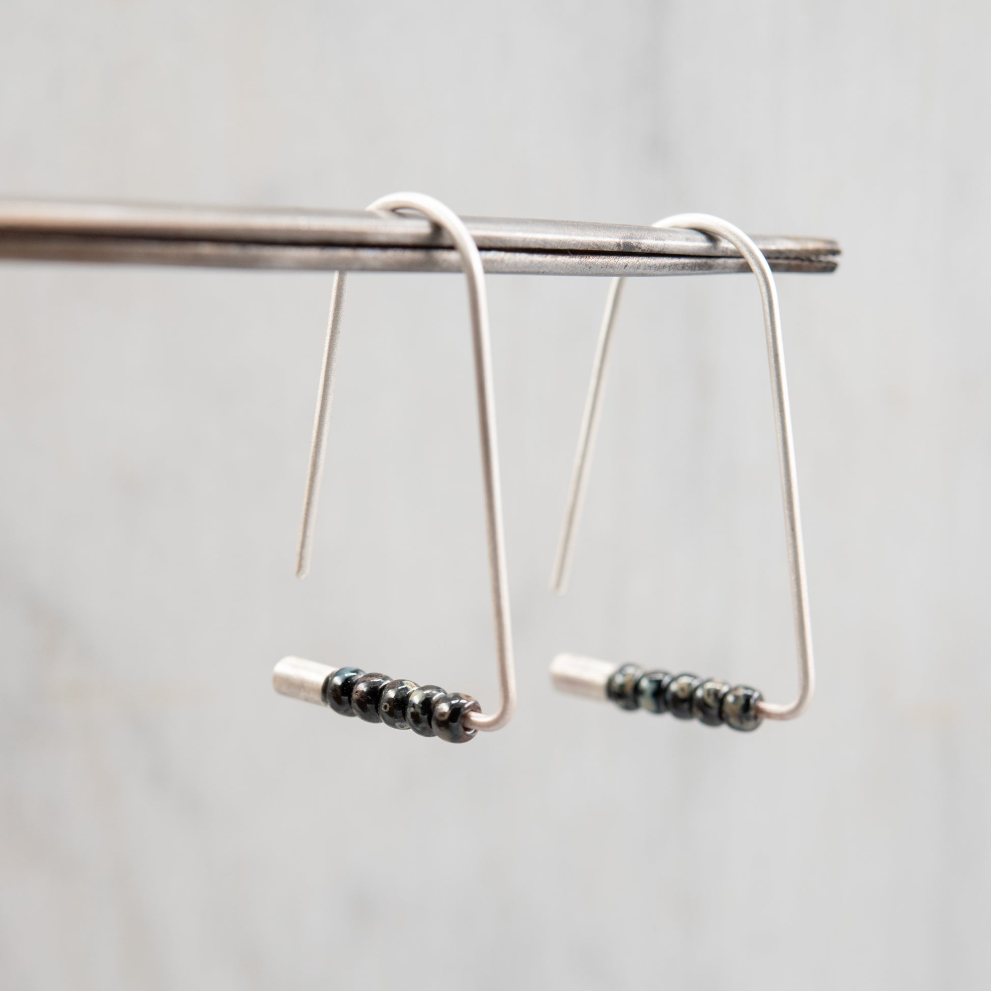 Boucles triangulaires légères en argent sterling avec perles Miyuki, suspendues et montrant leur mouvement.
