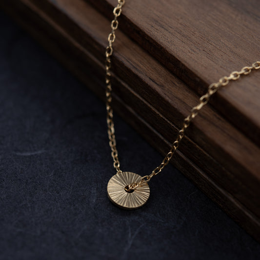Collier Soleil en vermeil avec pendentif rond gravé à la main, photographié en gros plan pour révéler la texture lumineuse du bijou fabriqué à Paris.