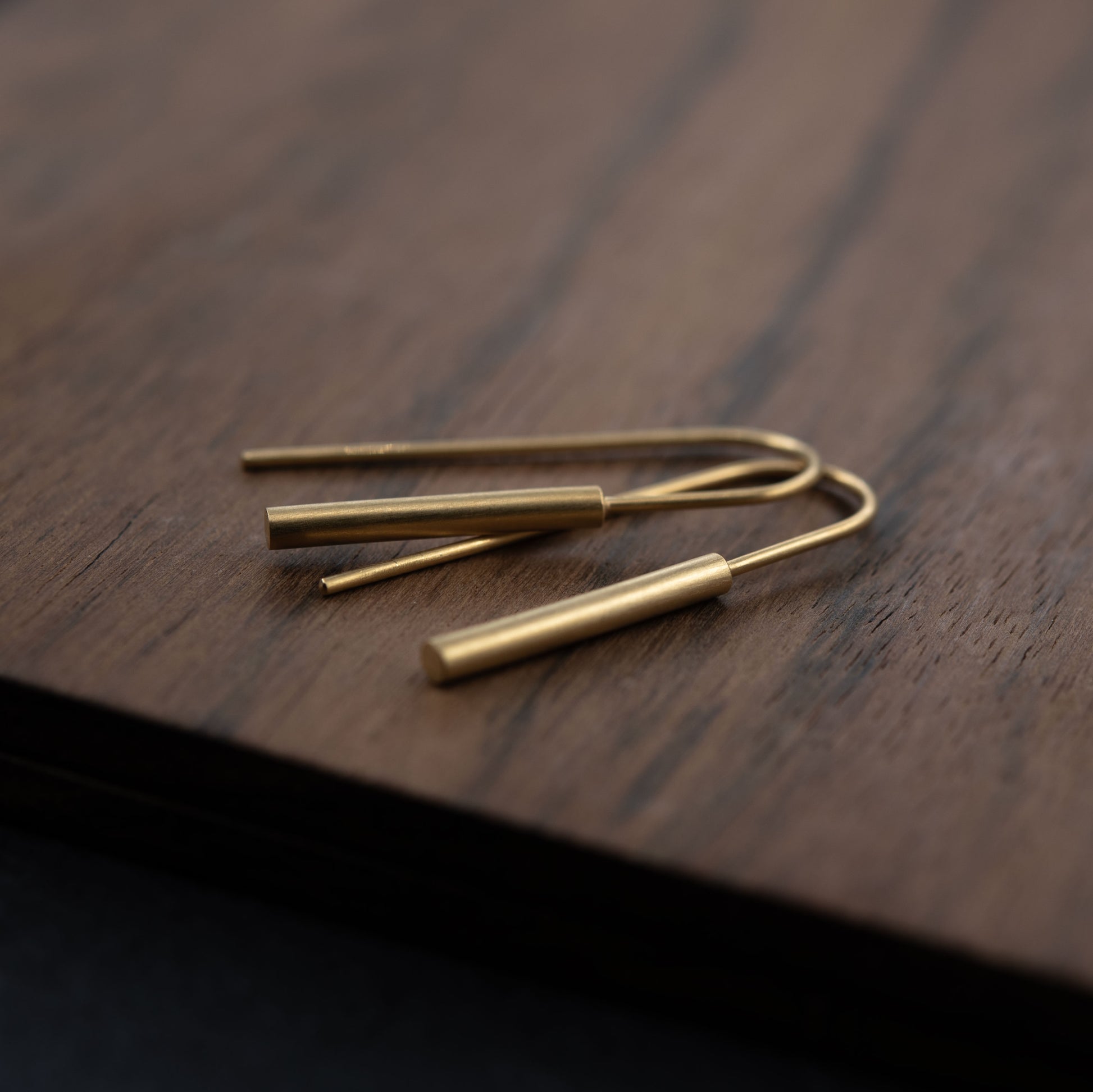 Gold threader earrings in vermeil displayed on dark wood and black surface, sleek matte finish and minimalist design in 24k gold-plated sterling silver