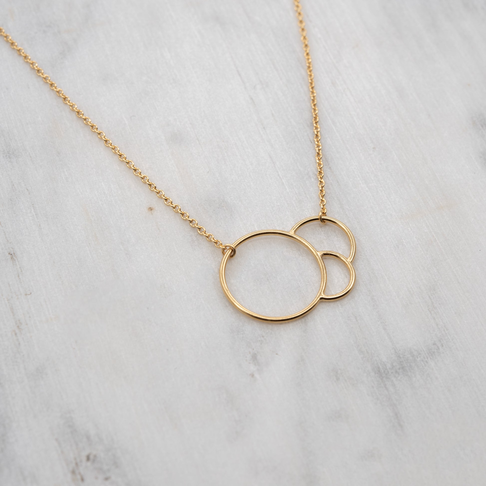 Gold necklace with interlaced circles on a marble surface