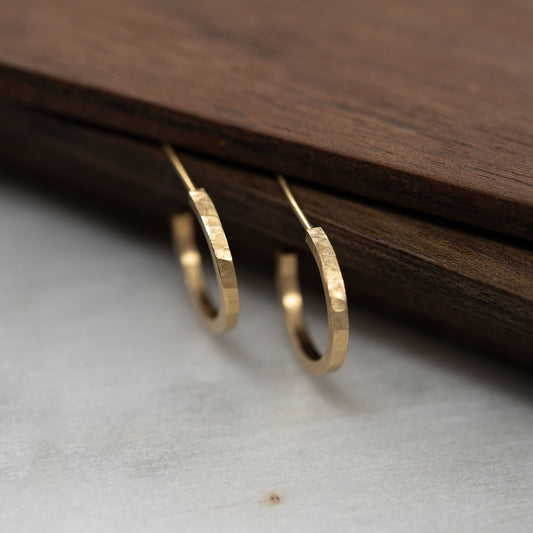 Hammered gold hoop earrings on a wooden surface. 