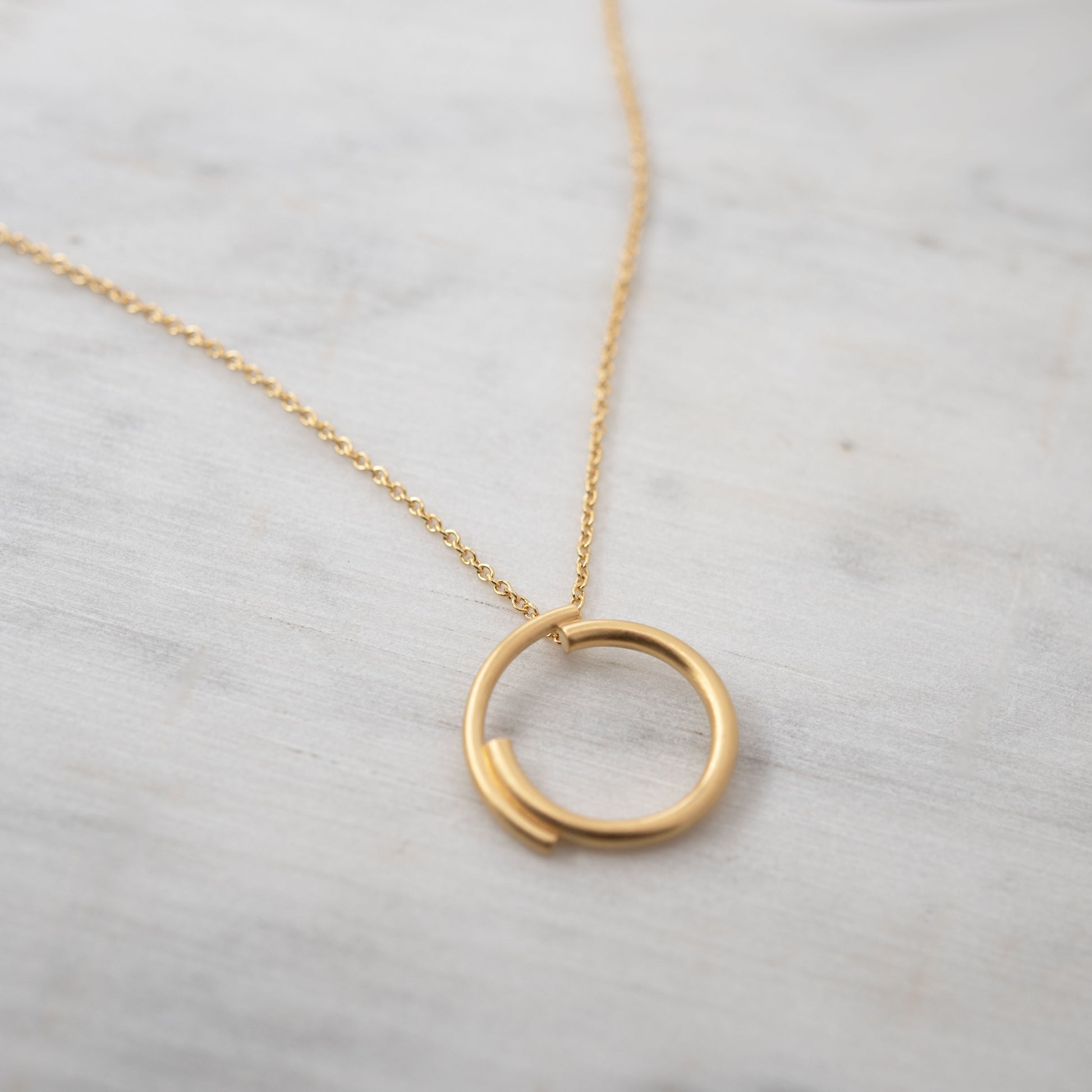 Close-up of a handmade vermeil circle necklace on a light background, minimalist Parisian jewelry.