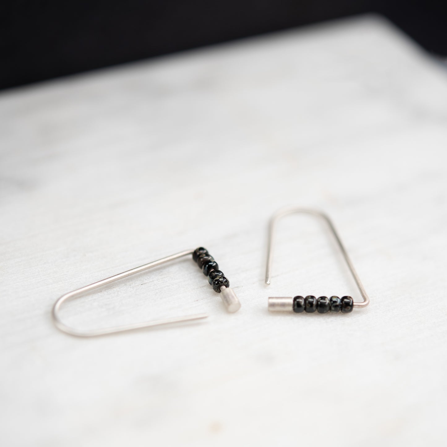Minimalist silver triangle earrings with black Miyuki beads photographed in natural light.