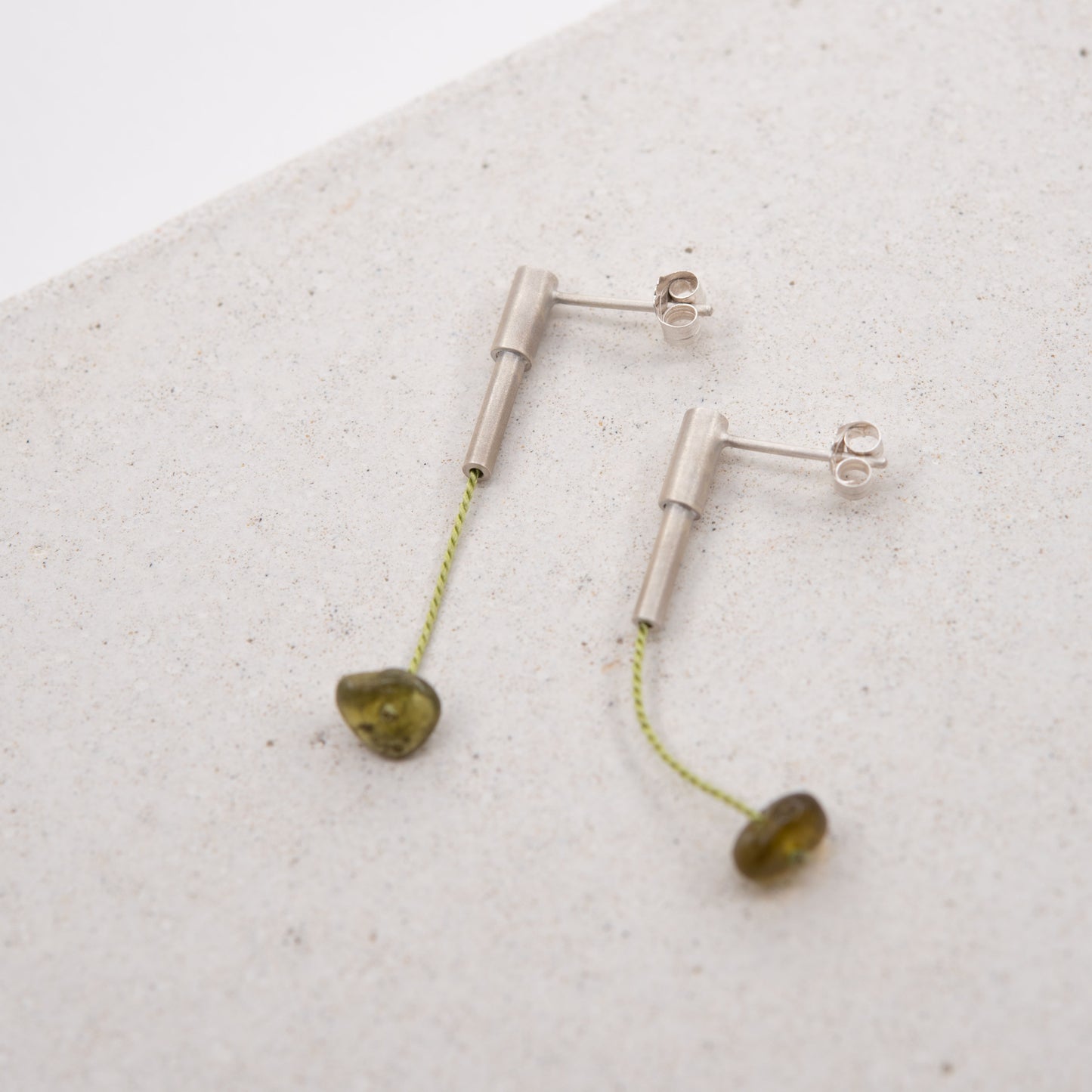 Pair of 37 millimeters length pendant earrings handmade in in Paris by A g J c  from  tube of matte sterling silver with a light green silk cord threaded through the center for hanging a green garnet stone.