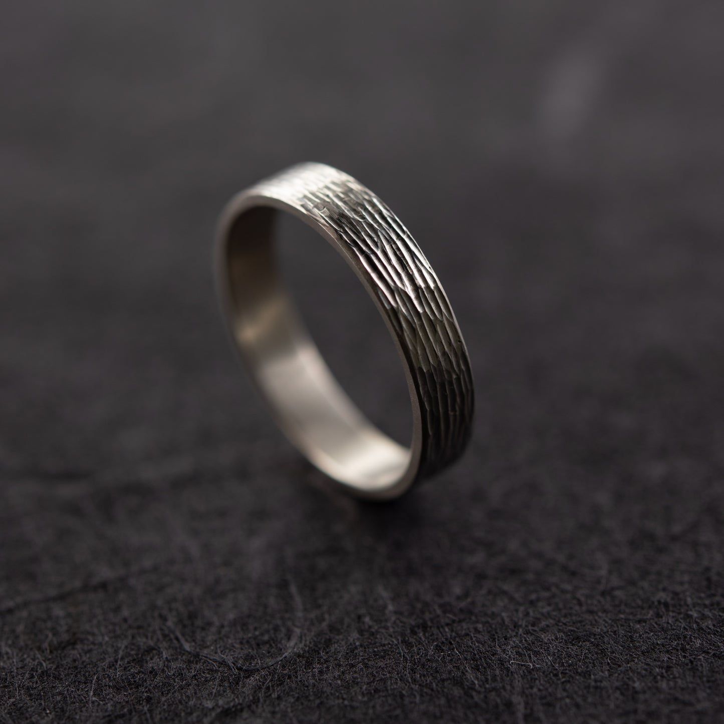 Gros plan sur la texture gravée à la main de la bague Étincelles en argent massif sur fond sombre, montrant la surface gravée brillante.