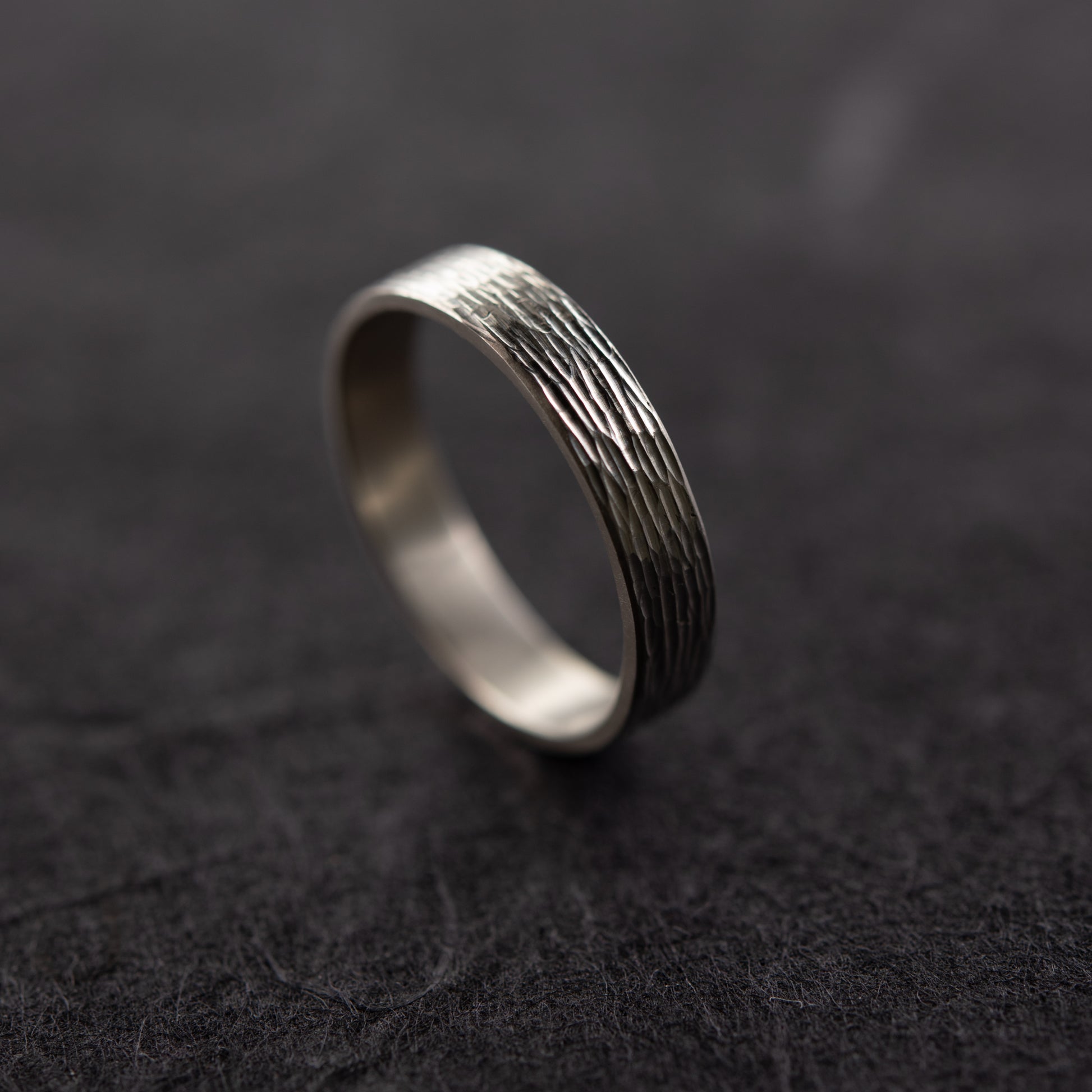 Gros plan sur la texture gravée à la main de la bague Étincelles en argent massif sur fond sombre, montrant la surface gravée brillante.