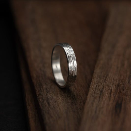 Vue latérale de la bague étincelles artisanale en argent avec relief gravé captant la lumière sur support en bois. Bijou fait main à Paris en argent massif texturé.
