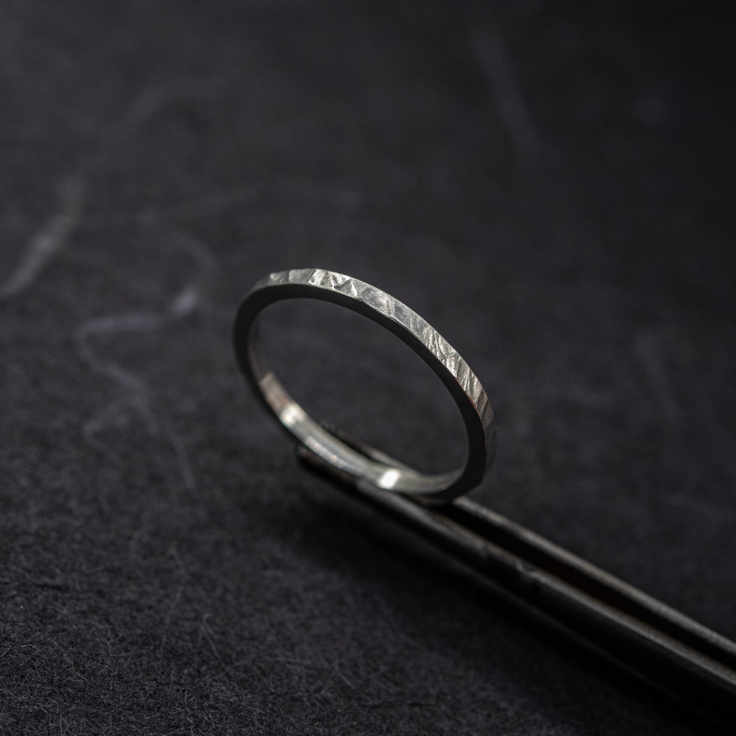 Bague martelée fine en argent massif 925 au fini facetté, photographiée sur un outil de bijoutier sur fond sombre.