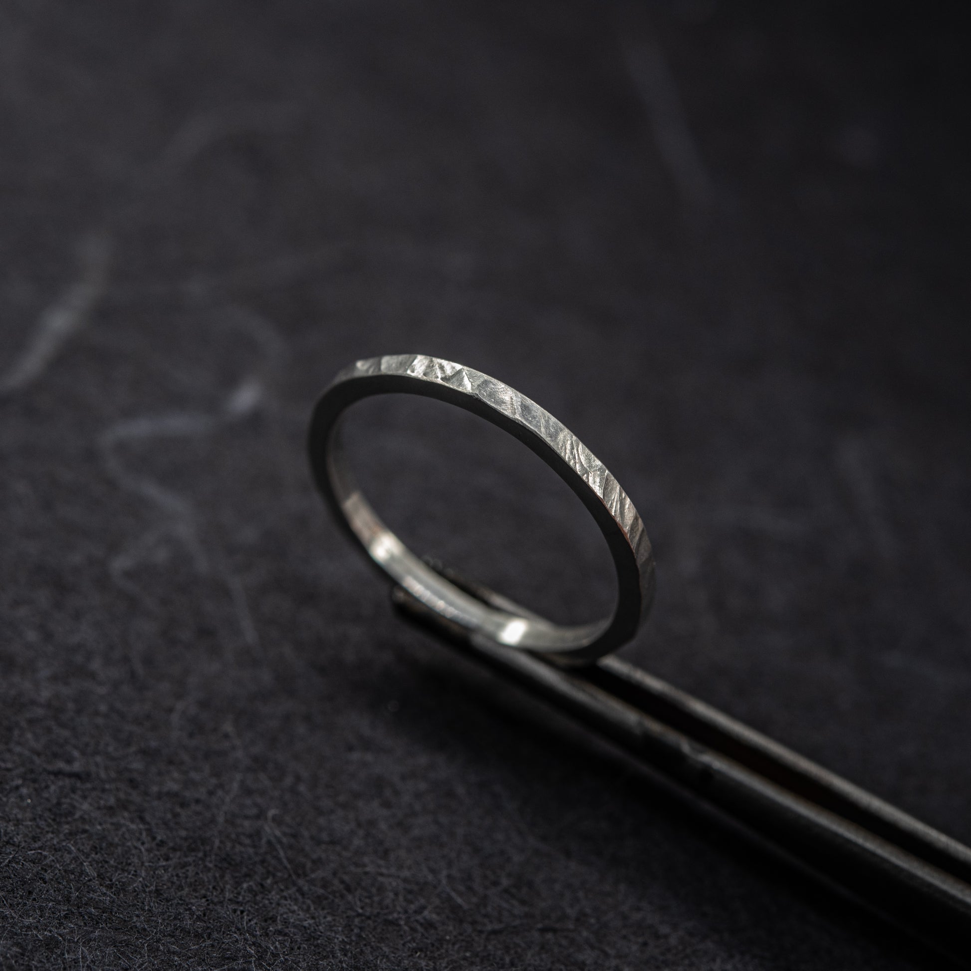 Bague martelée fine en argent massif 925 au fini facetté, photographiée sur un outil de bijoutier sur fond sombre.