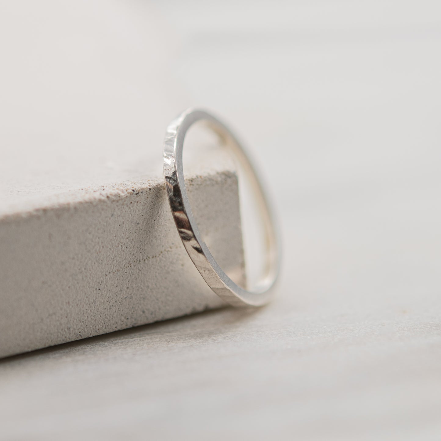 Vue rapprochée d'une bague martelée fine en argent massif 925 faite à la main à Paris, posée sur un support en béton clair.