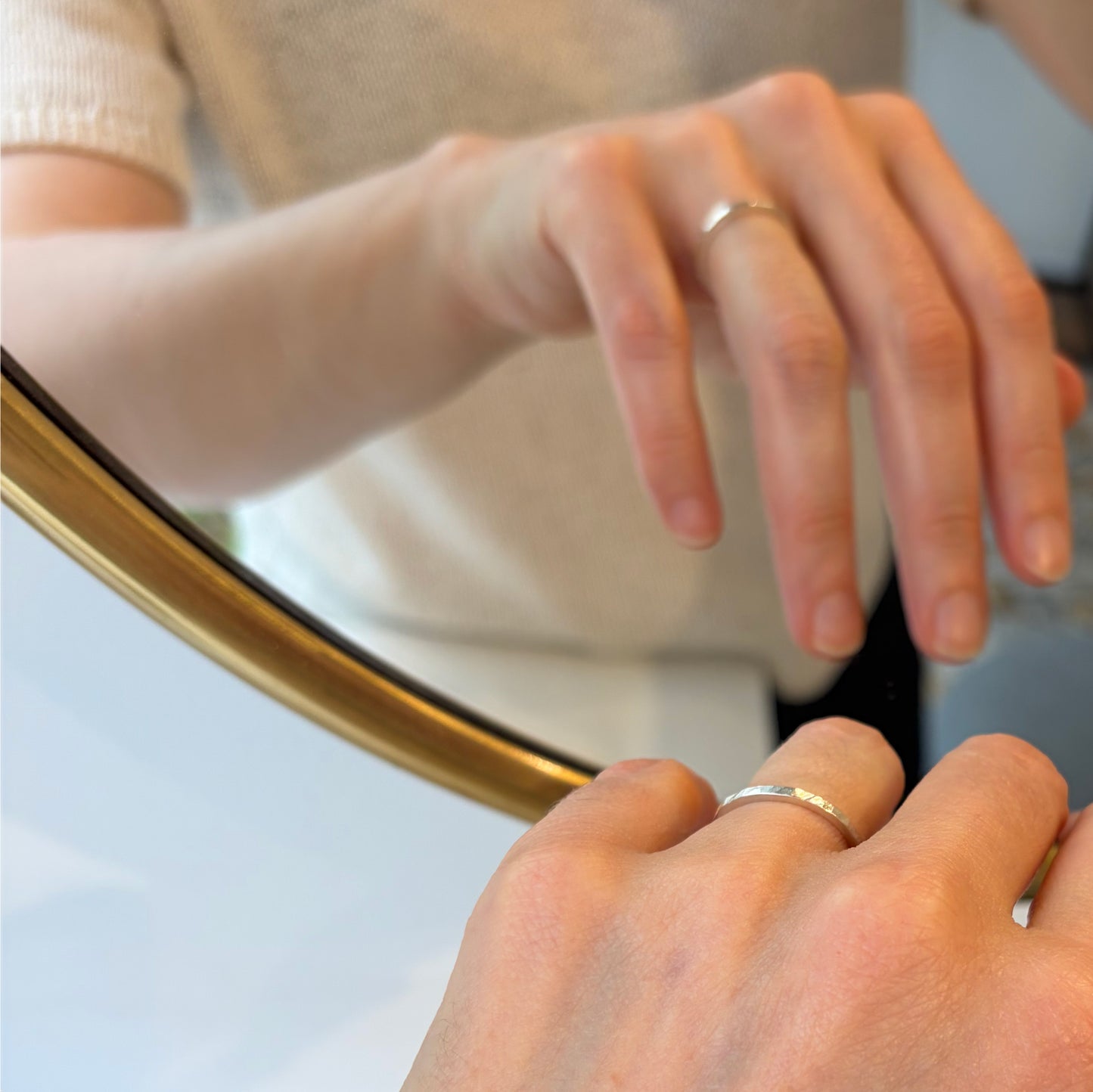 Vue rapprochée d'une personne portant une fine bague martelées$ en argent massif 925 devant un miroir au cadre doré.