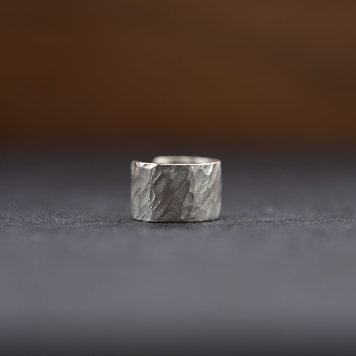 Vue de face de la bague d’oreille en argent massif artisanale, large surface martelée à la main sur fond sombre.
