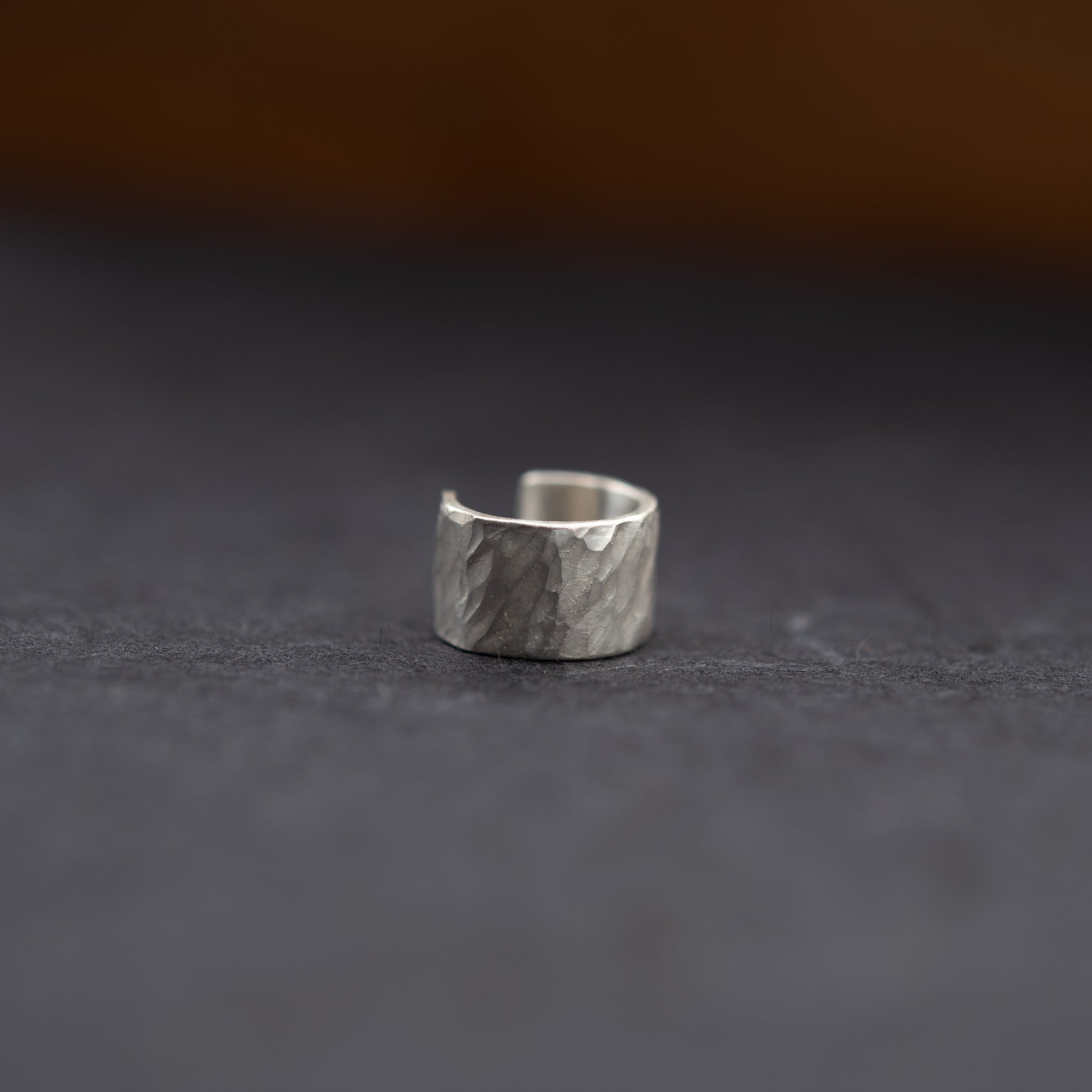 Gros plan de la bague d’oreille en argent massif, texture martelée artisanale sur fond sombre