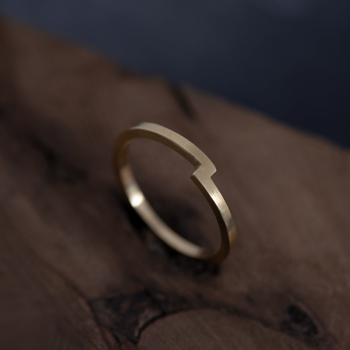Vue de trois quarts de la bague Rencontre en vermeil et de son point de rencontre, posée sur une surface en bois sombre texturé.