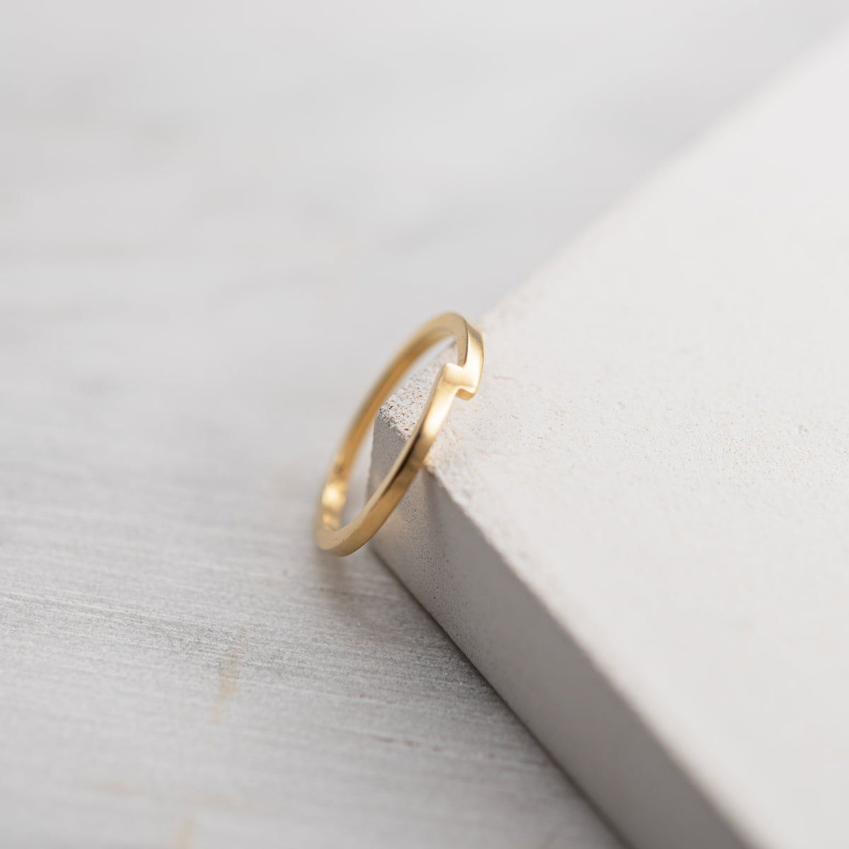 Bague minimaliste Rencontre en vermeil poli avec encoche graphique sur un support minéral clair.