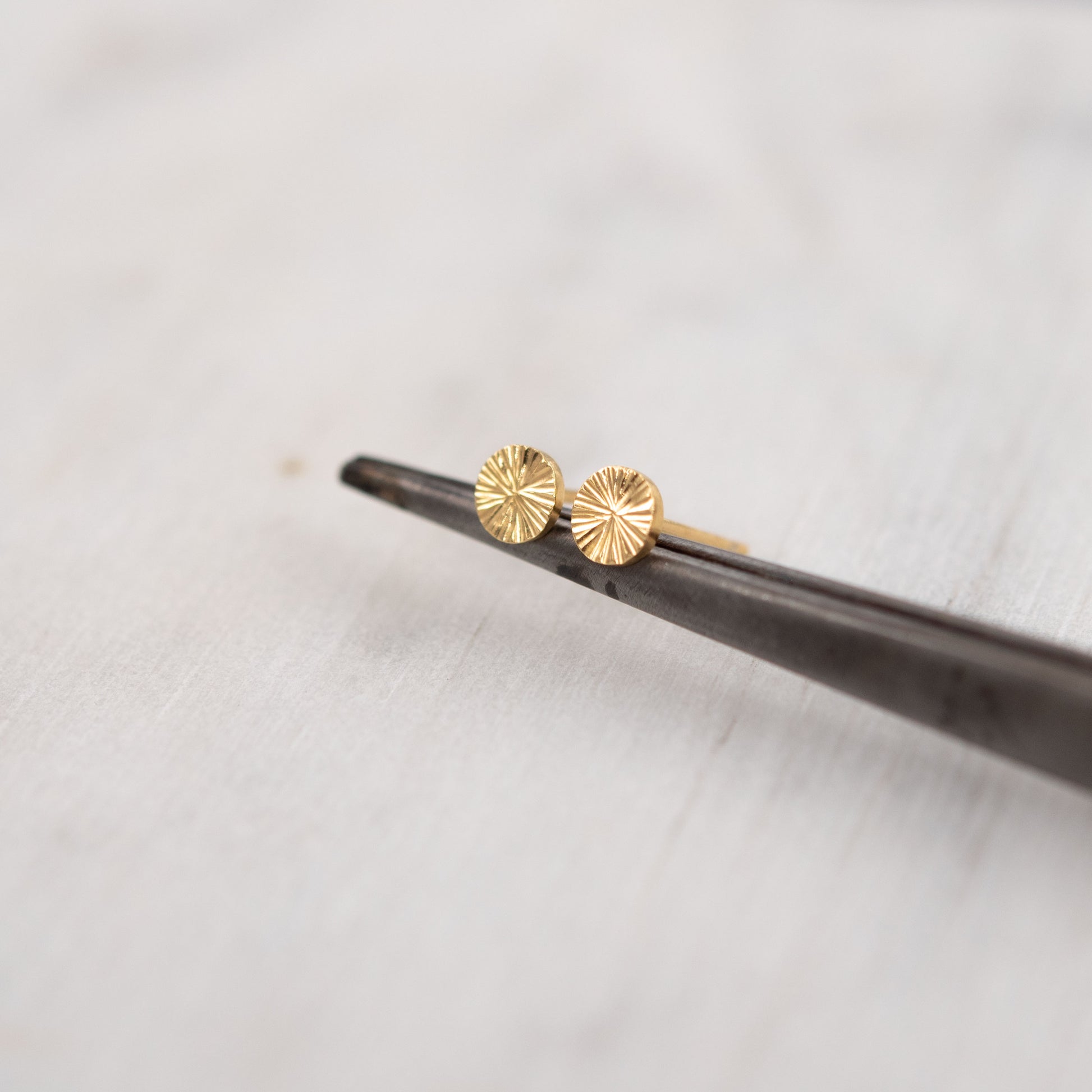Gros plan de petites boucles d’oreilles clous en vermeil or gravé sur fond blanc – bijou talisman minimaliste de Paris