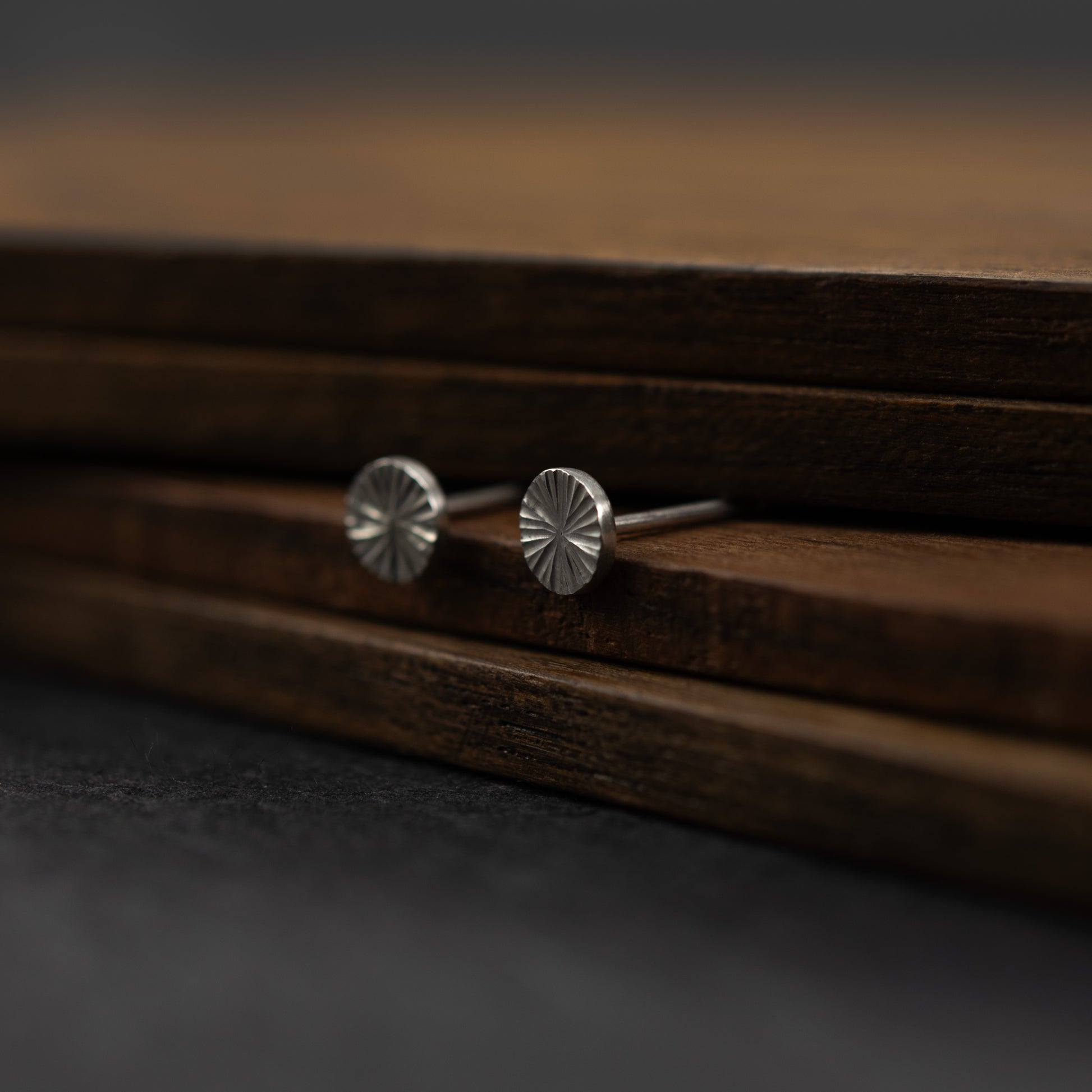 Puces d’oreilles en argent massif 5 mm avec surface gravée et éclat lumineux sur une surface de bois foncé. 