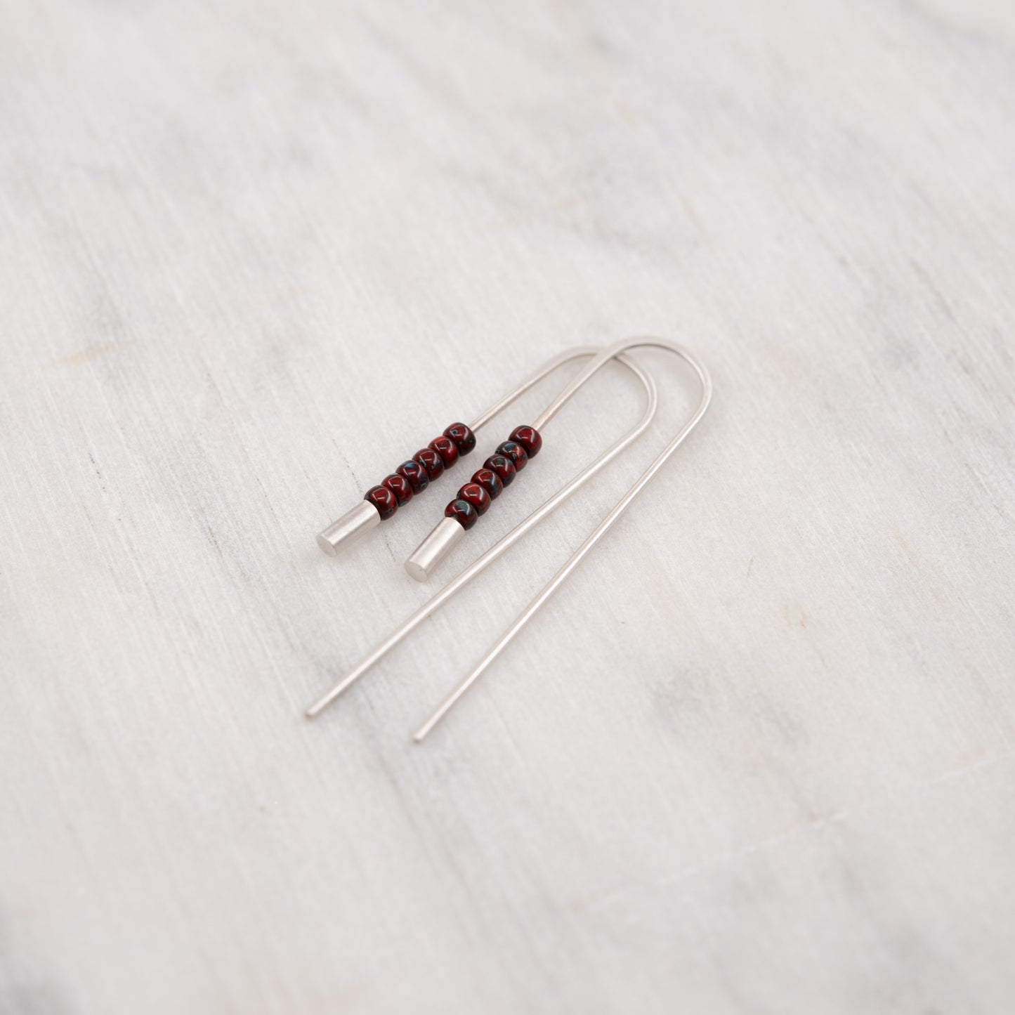 Gros plan des boucles d’oreilles traversantes artisanales en argent et perles rouges Miyuki sur fond clair