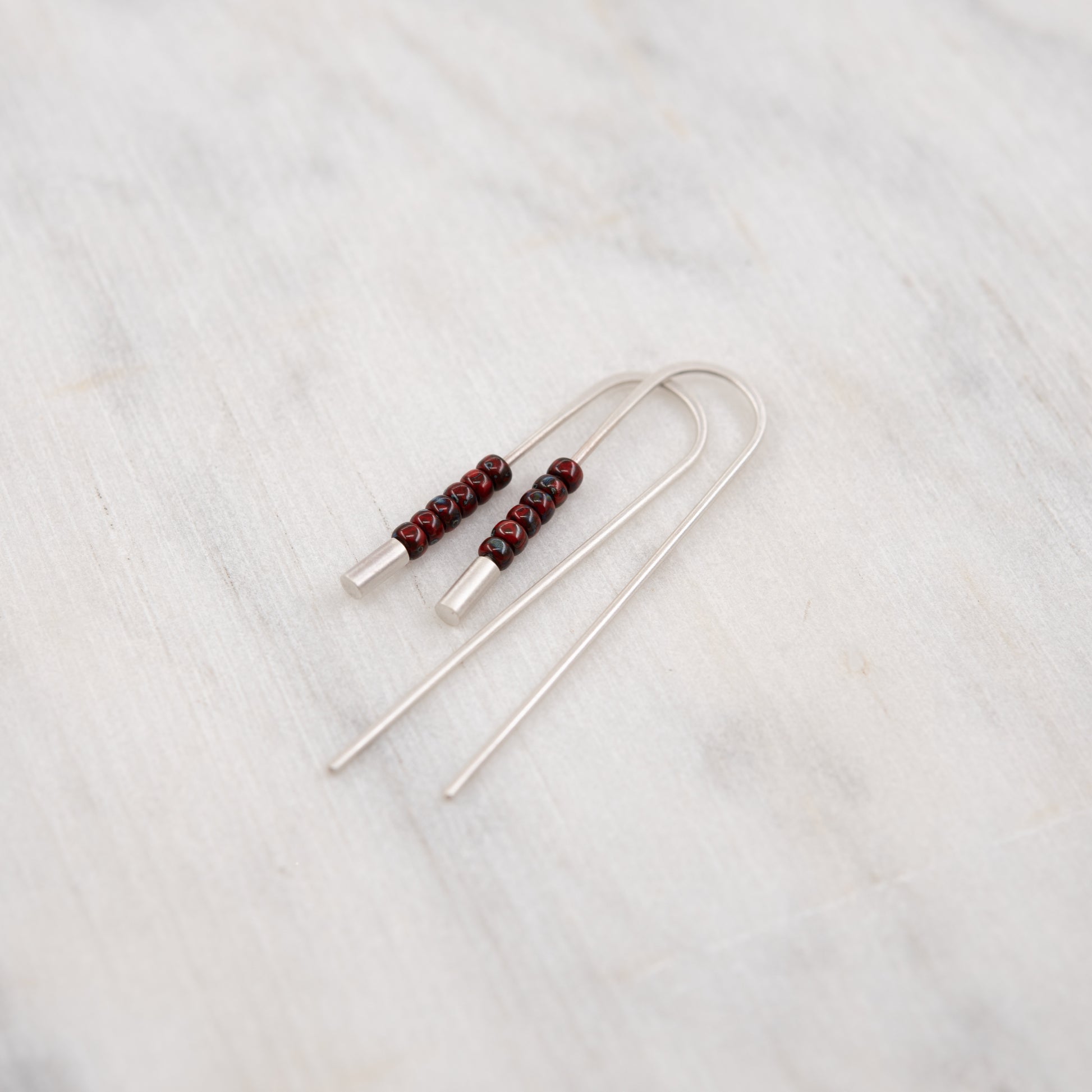 Gros plan des boucles d’oreilles traversantes artisanales en argent et perles rouges Miyuki sur fond clair