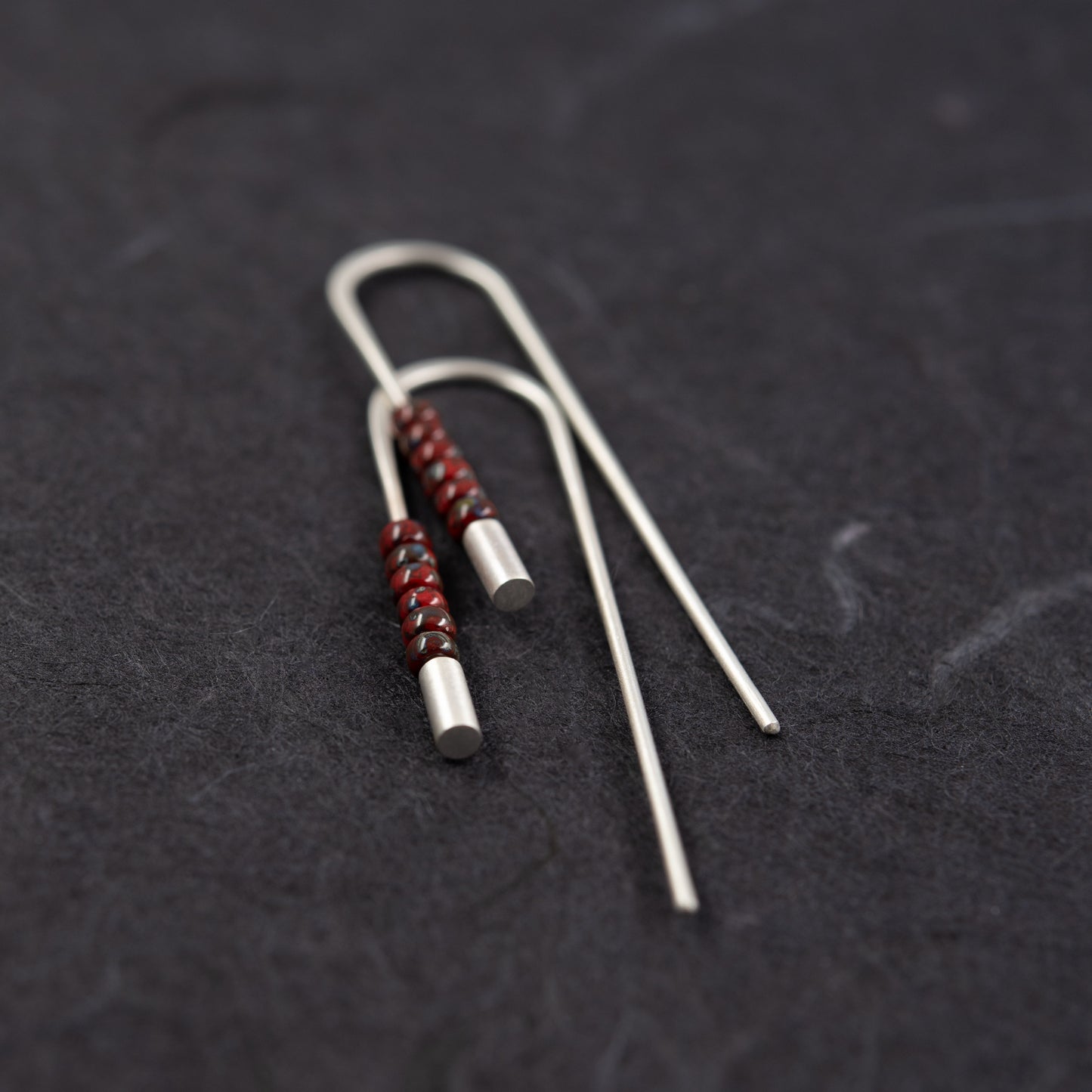 Vue rapprochée de la paire de boucles traversantes en argent 925 avec perles rouges Miyuki et extrémités brossées sur fond sombre