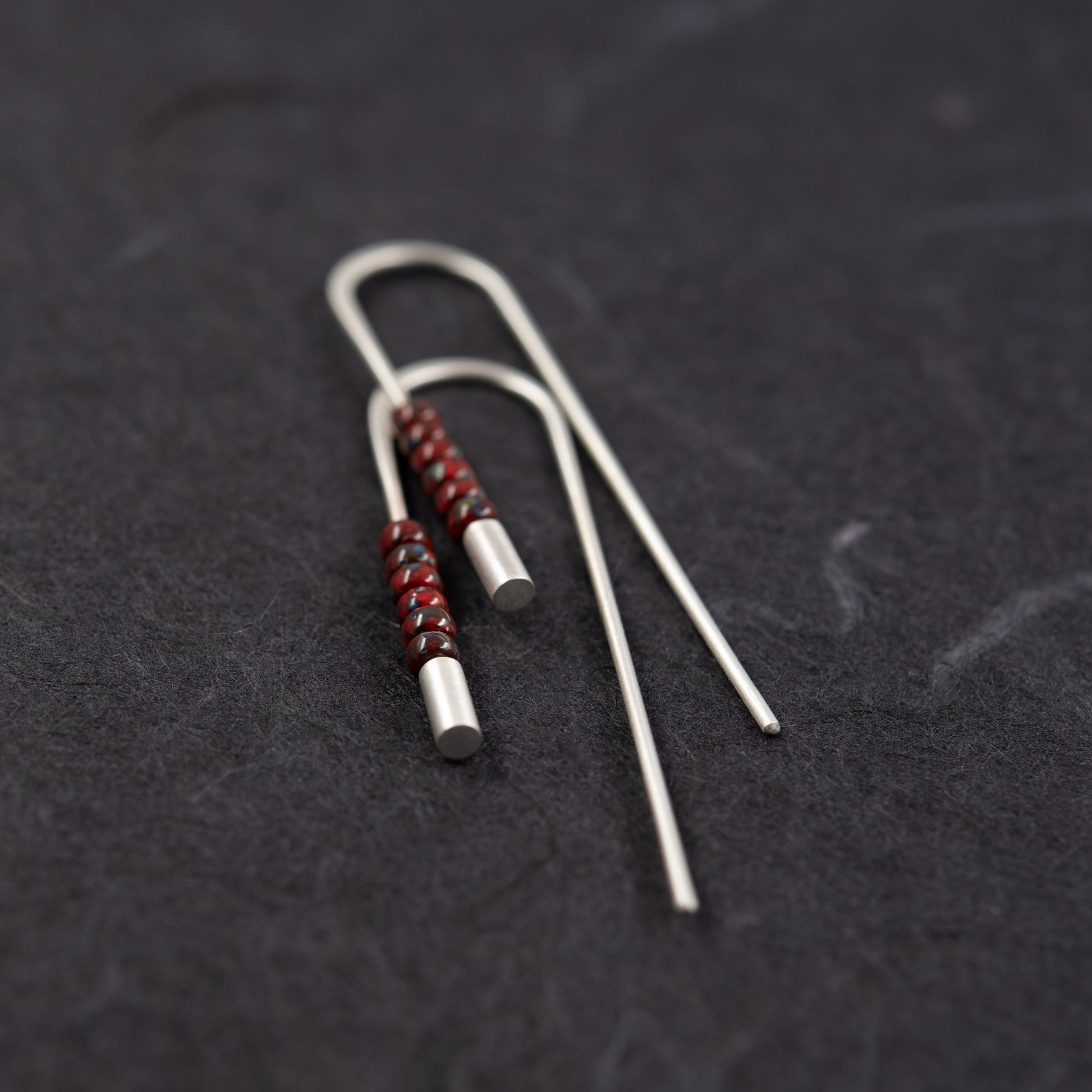 Vue rapprochée de la paire de boucles traversantes en argent 925 avec perles rouges Miyuki et extrémités brossées sur fond sombre