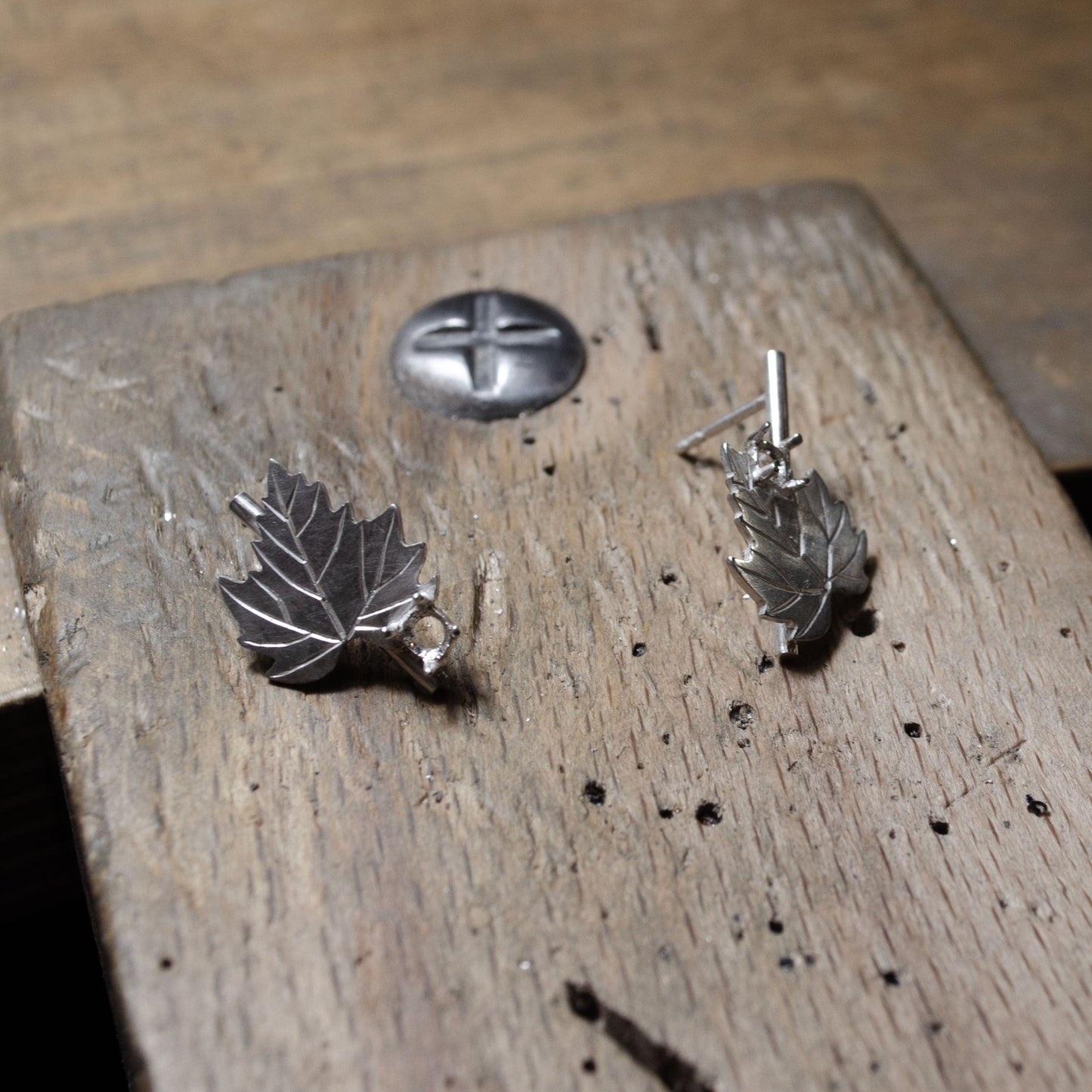 Gros plan sur des boucles d'oreilles en argent en forme de feuille, en train d'être fabriquées sur une table en bois.