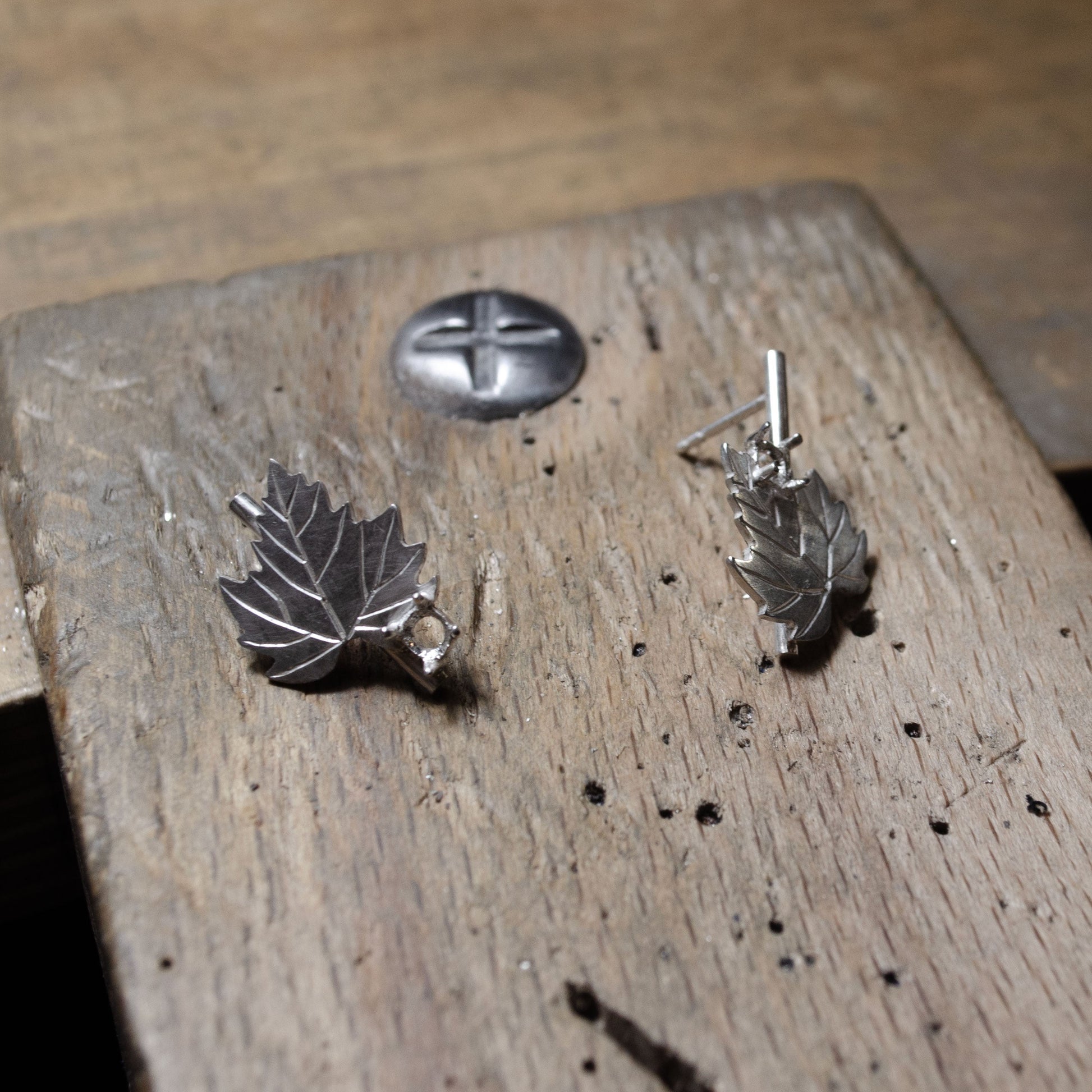 Gros plan sur des boucles d'oreilles en argent en forme de feuille, en train d'être fabriquées sur une table en bois.