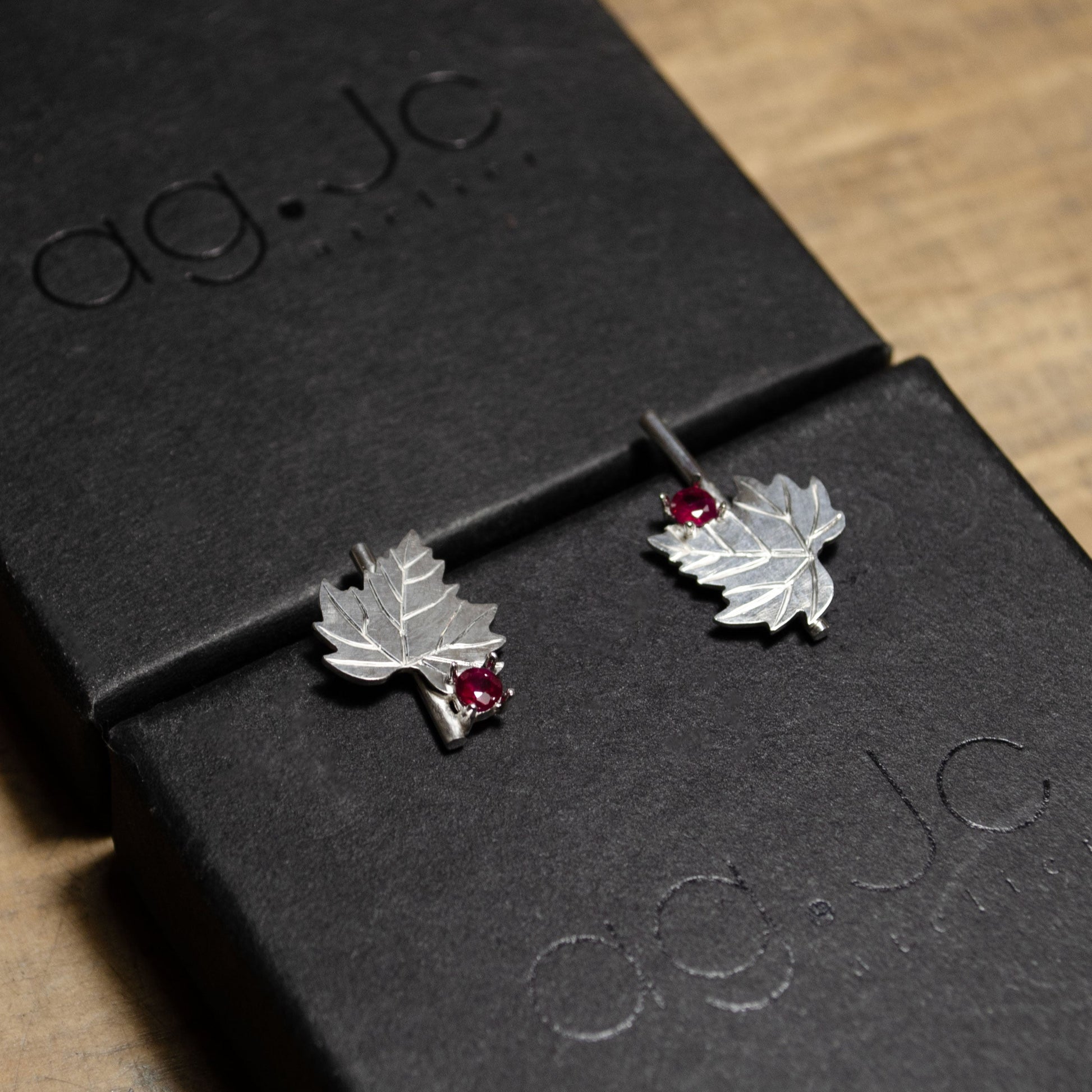 Vue rapprochée de boucles d'oreilles en argent, conçues sous la forme de feuilles, en cours de fabrication sur une surface en bois.