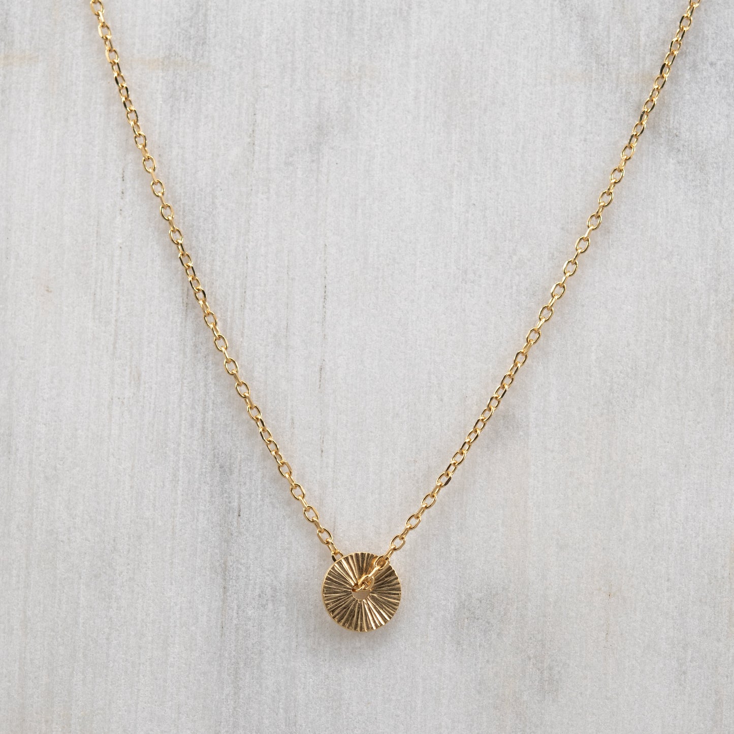 Vue de face du collier Soleil en vermeil or avec un pendentif rond gravé à la main et une fine chaîne en vermeil. Bijou artisanal fabriqué à Paris.