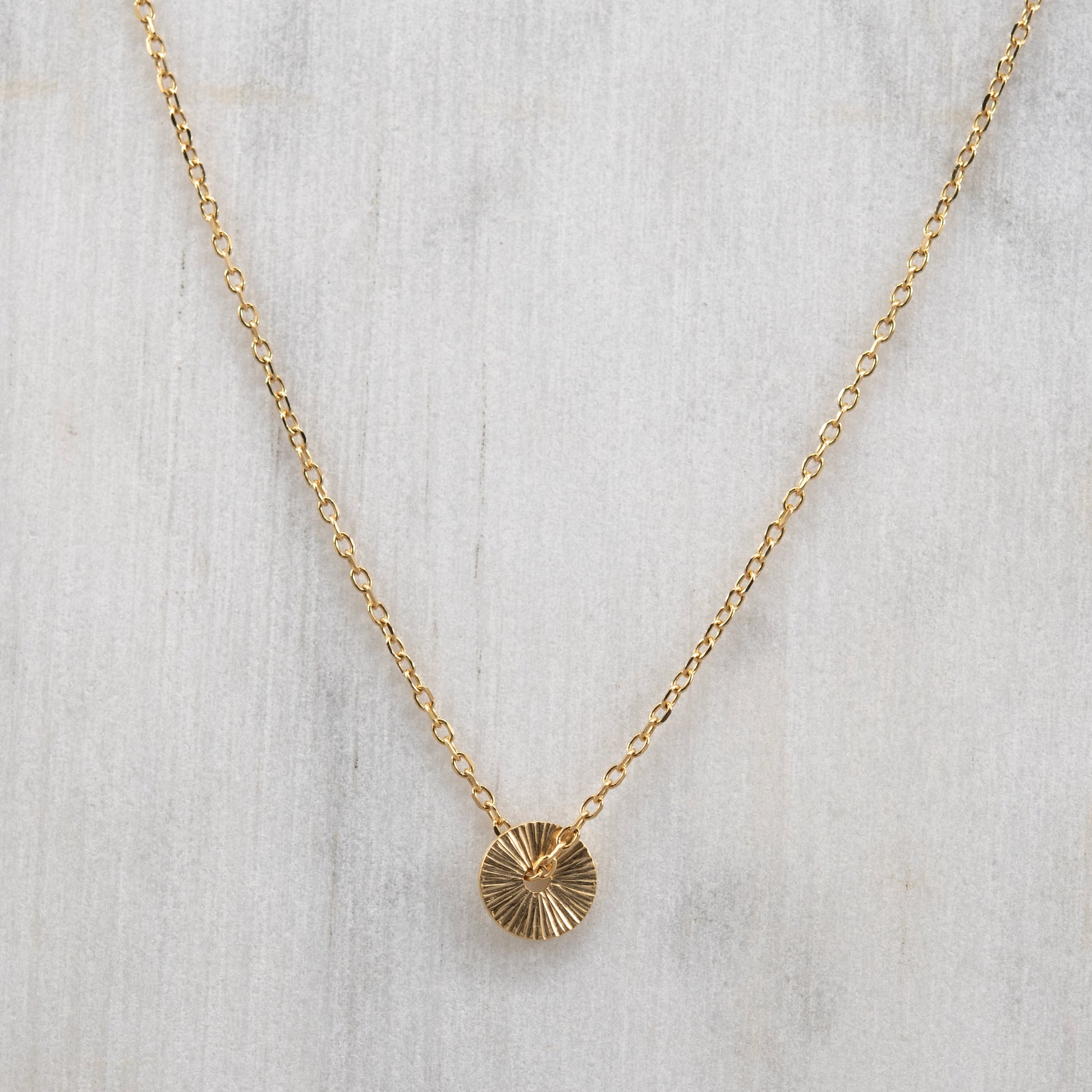 Vue de face du collier Soleil en vermeil or avec un pendentif rond gravé à la main et une fine chaîne en vermeil. Bijou artisanal fabriqué à Paris.