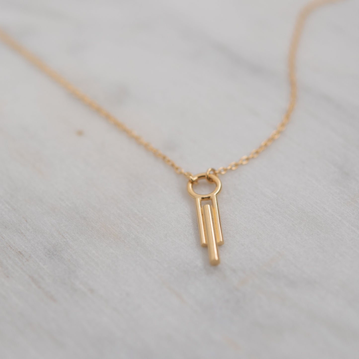 Gros plan d'un pendentif et chaîne de collier cylindrique Art Déco en vermeil sur marbre blanc, bijou minimaliste fait main
