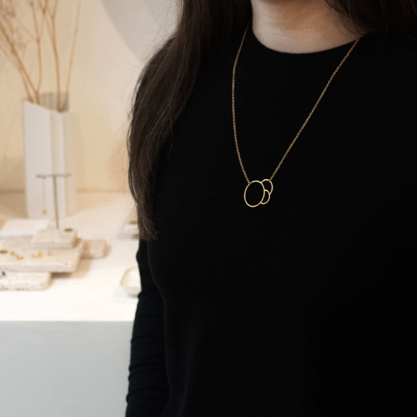 Femme portant un collier en or avec des anneaux entrelacés dans un cadre intérieur flou.