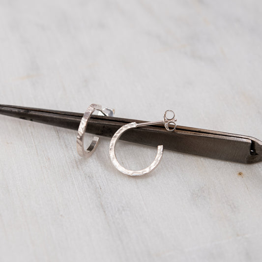 Paire de créoles en argent massif 925 martelé posée sur un outil en métal sombre, sur un fond en marbre gris clair.