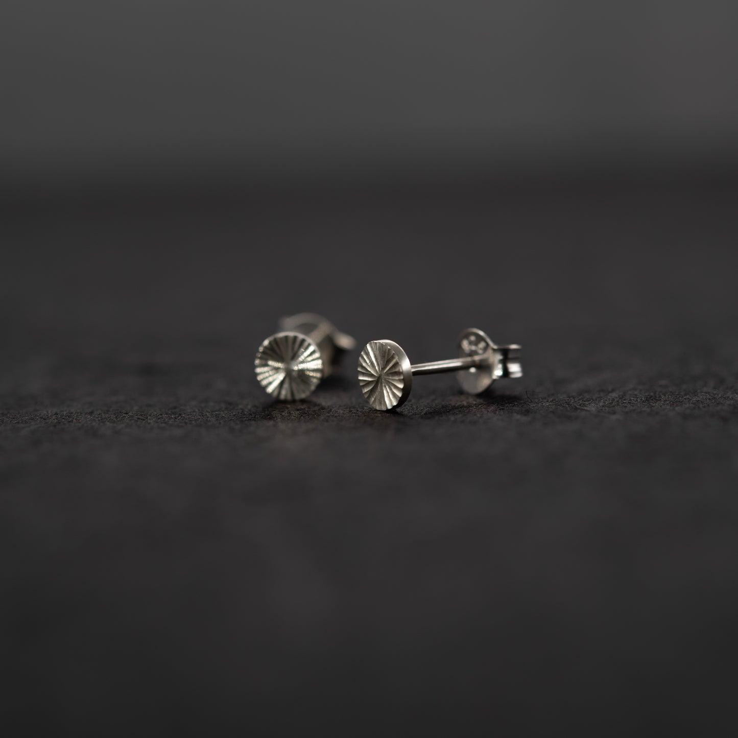 Gros plan sur des puces d’oreilles en argent massif gravées à la main, motif lumineux sur une surface grise