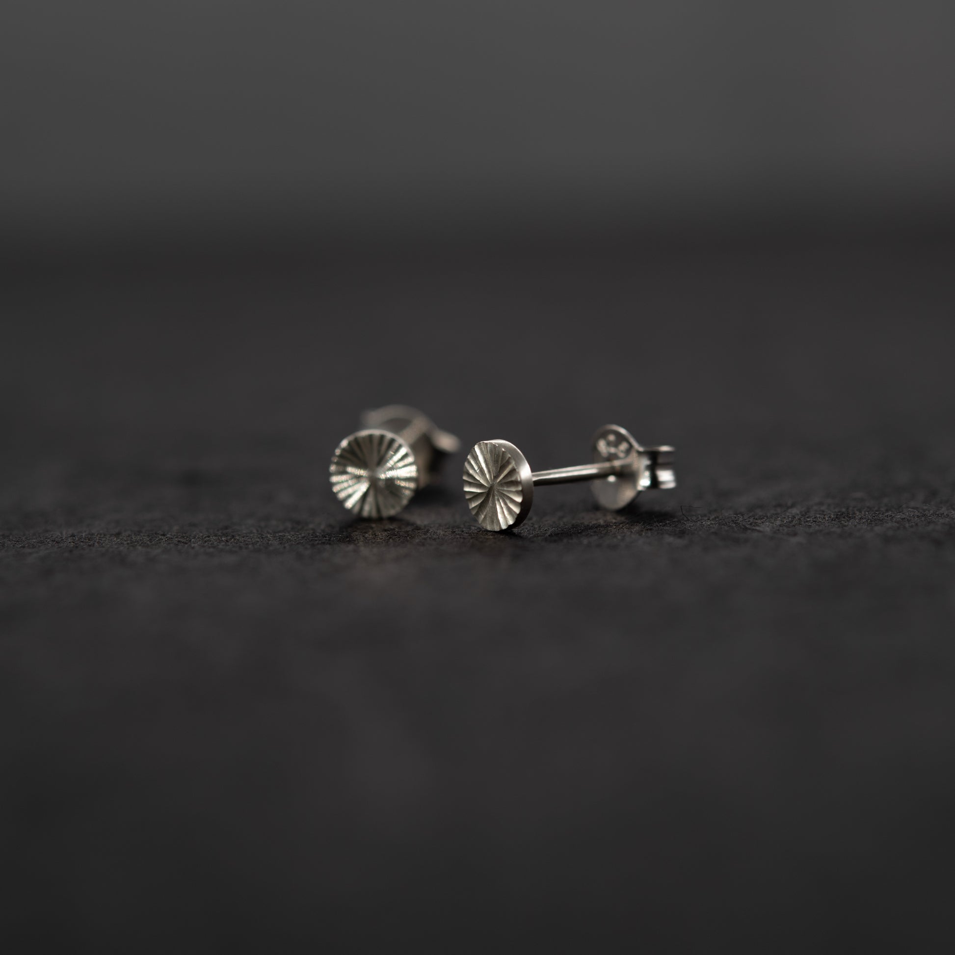 Gros plan sur des puces d’oreilles en argent massif gravées à la main, motif lumineux sur une surface grise