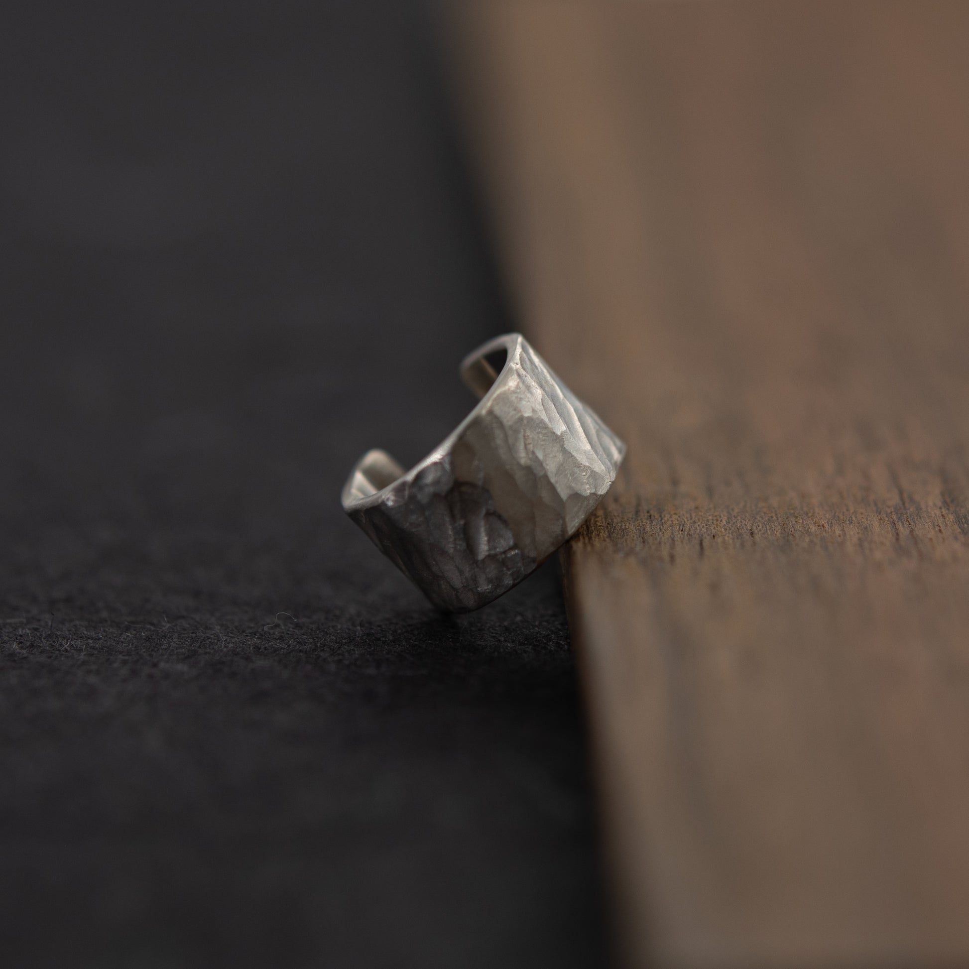 Vue trois-quarts de la bague d’oreille en argent massif martelé, posée près du bois sur fond sombre.