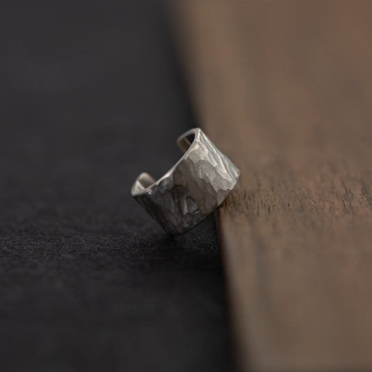 Vue trois-quarts de la bague d’oreille en argent massif martelé, posée près du bois sur fond sombre.