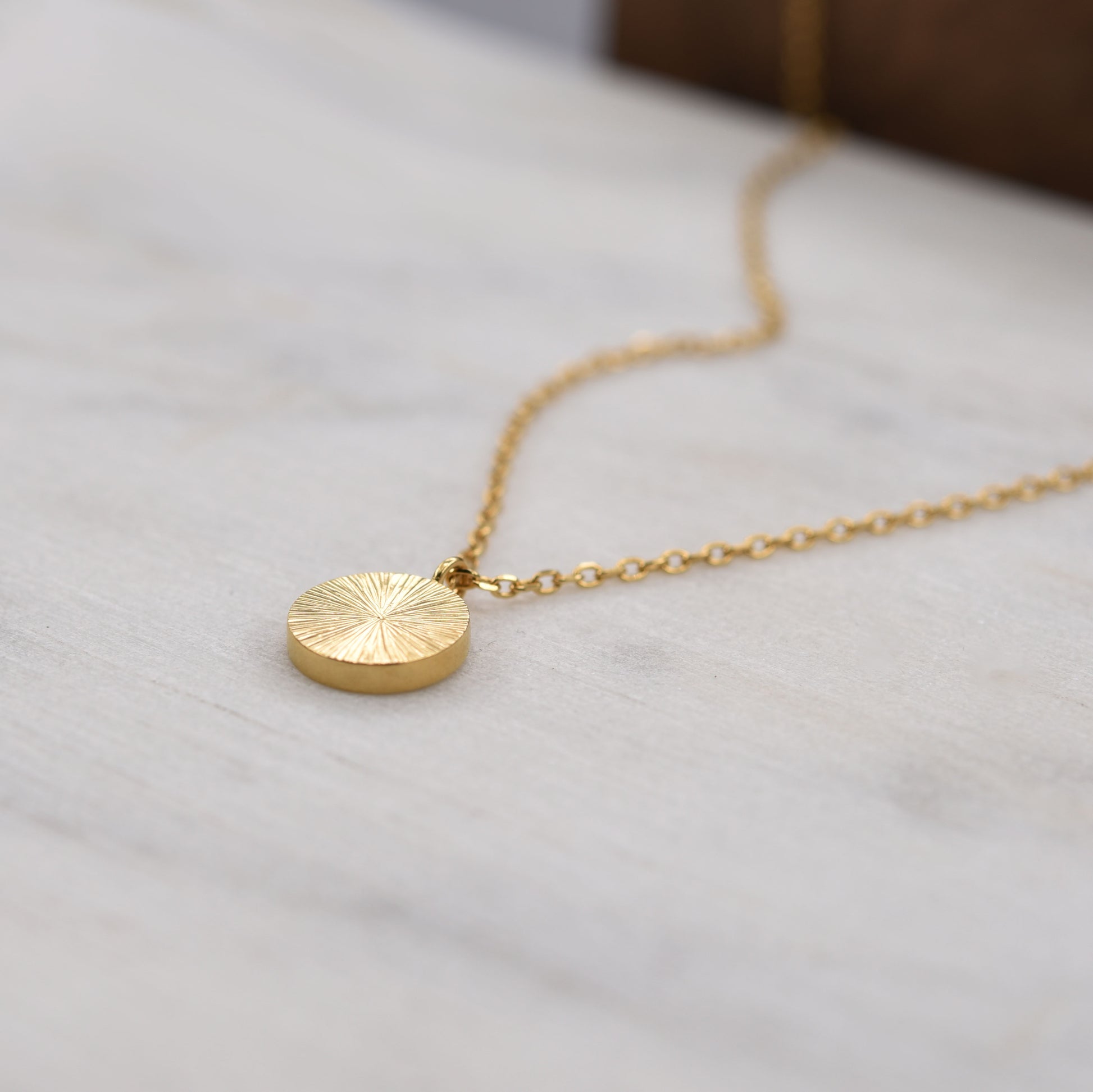 Side angle of gold vermeil sunburst pendant necklace, minimalist artisan jewelry from Paris.