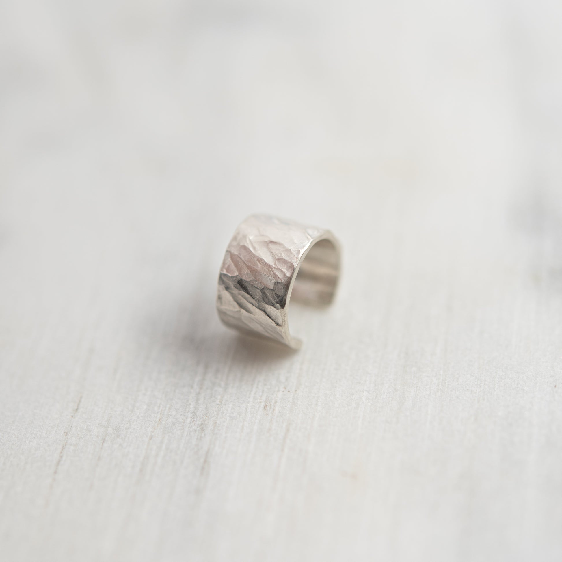 Three-quarter view of hammered sterling silver ear cuff, hand-textured surface on light background.