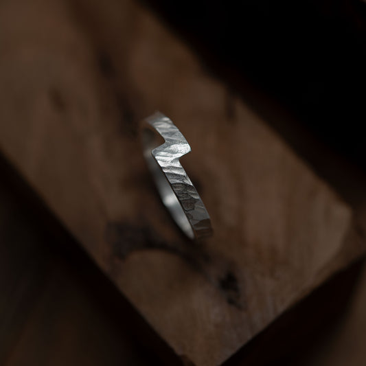 Close-up of a handmade hammered Unity ring crafted from sterling silver. The ring features a unique zigzag design and is showcased on a textured wooden surface, emphasizing its artisanal quality. Designed and made in Paris, this ring represents the concept of unity and is perfect for meaningful occasions.