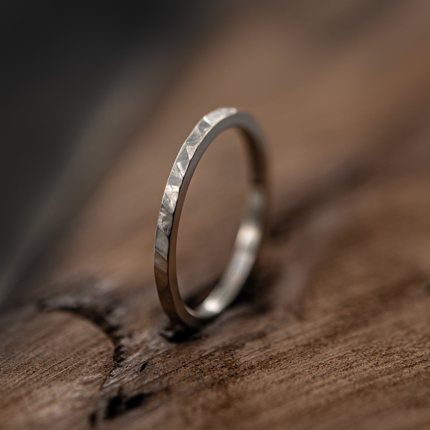 A silver band ring with a textured, hammered finish resting on a rustic wooden surface.