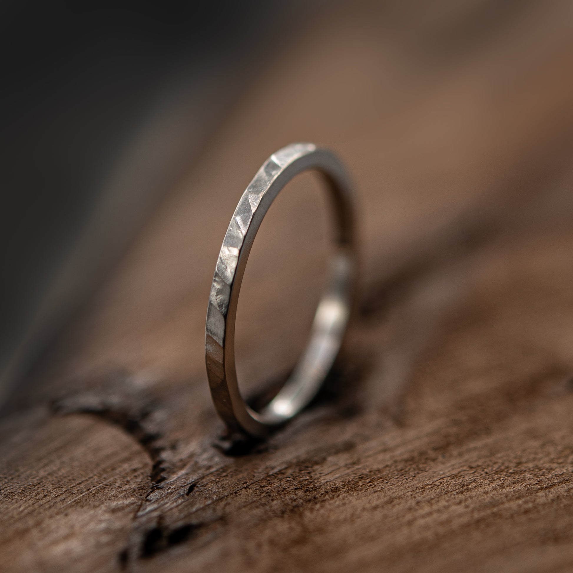A silver band ring with a textured, hammered finish resting on a rustic wooden surface.