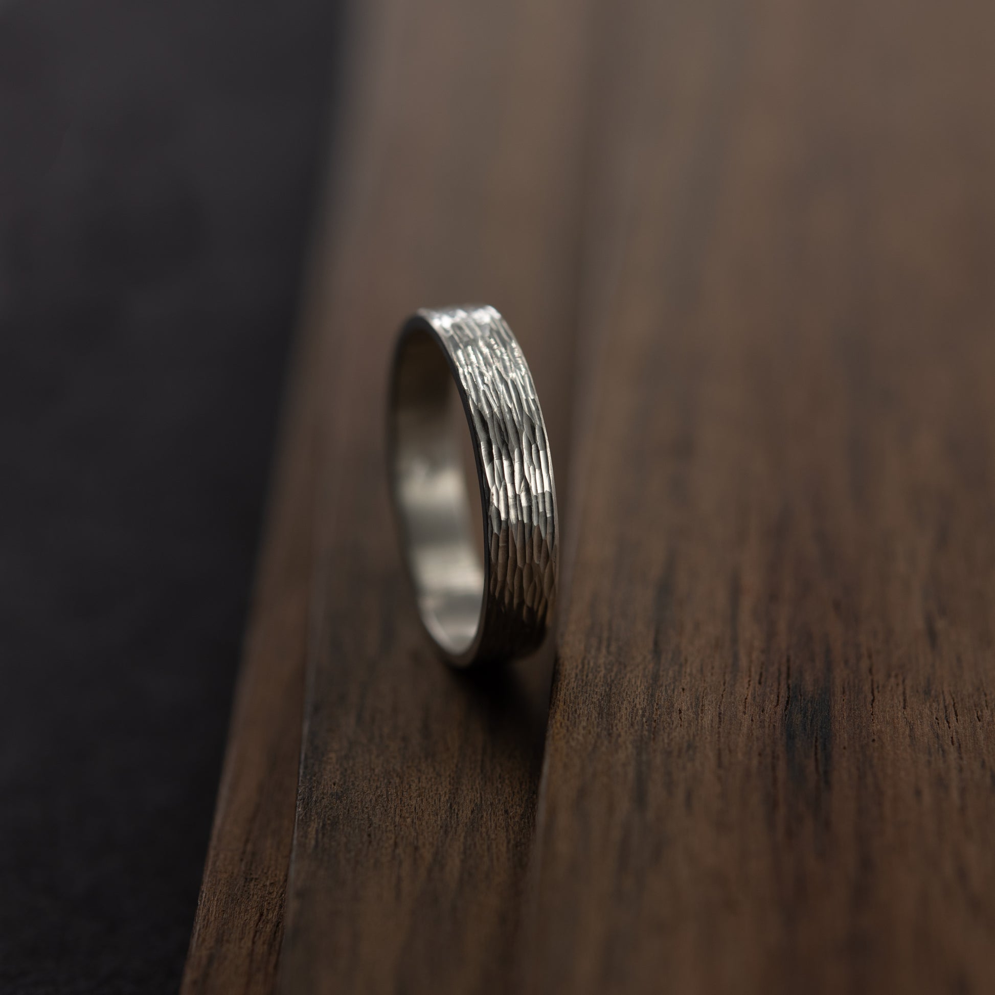 Close-up of hand-engraved texture silver band ring displayed on dark wooden surface. Handmade in Paris by AgJc