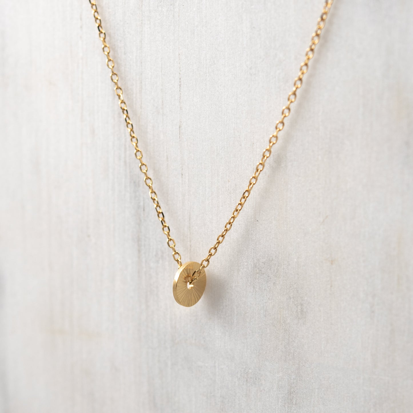 Close-up of the hand-engraved gold vermeil sun pendant highlighting its radiant texture and fine chain on a white backgroung.
