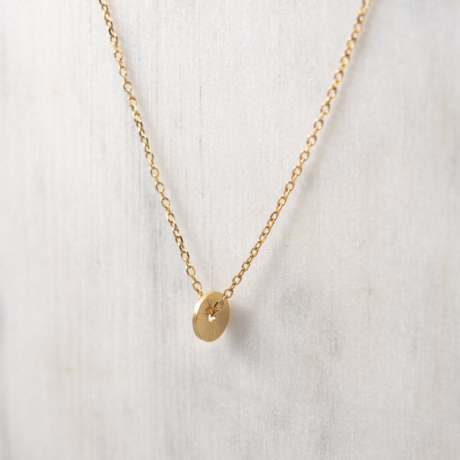 Close-up of the hand-engraved gold vermeil sun pendant highlighting its radiant texture and fine chain on a white backgroung.