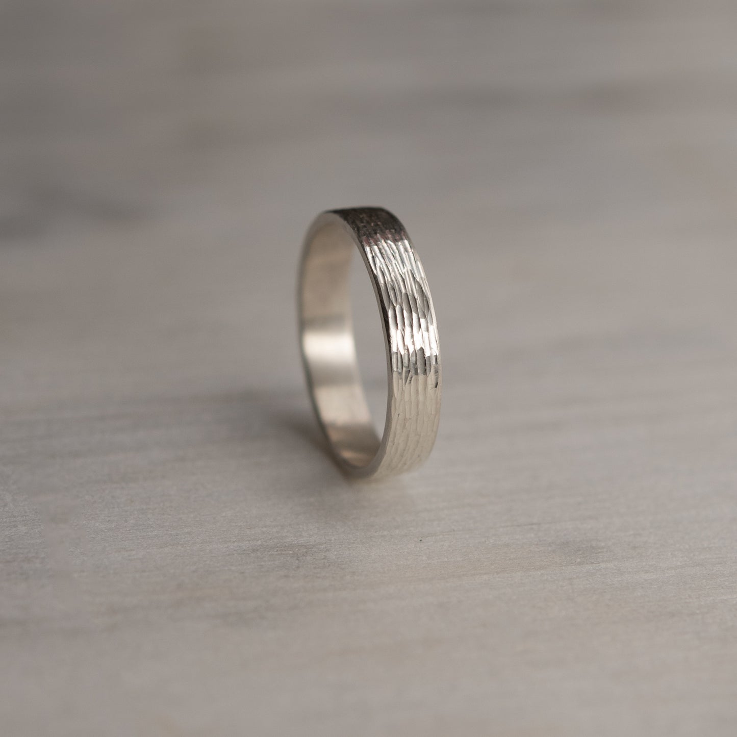 Hand-textured, light reflecting silver ring standing upright on a soft background, minimalist product view. Handmade in Paris by AgJc