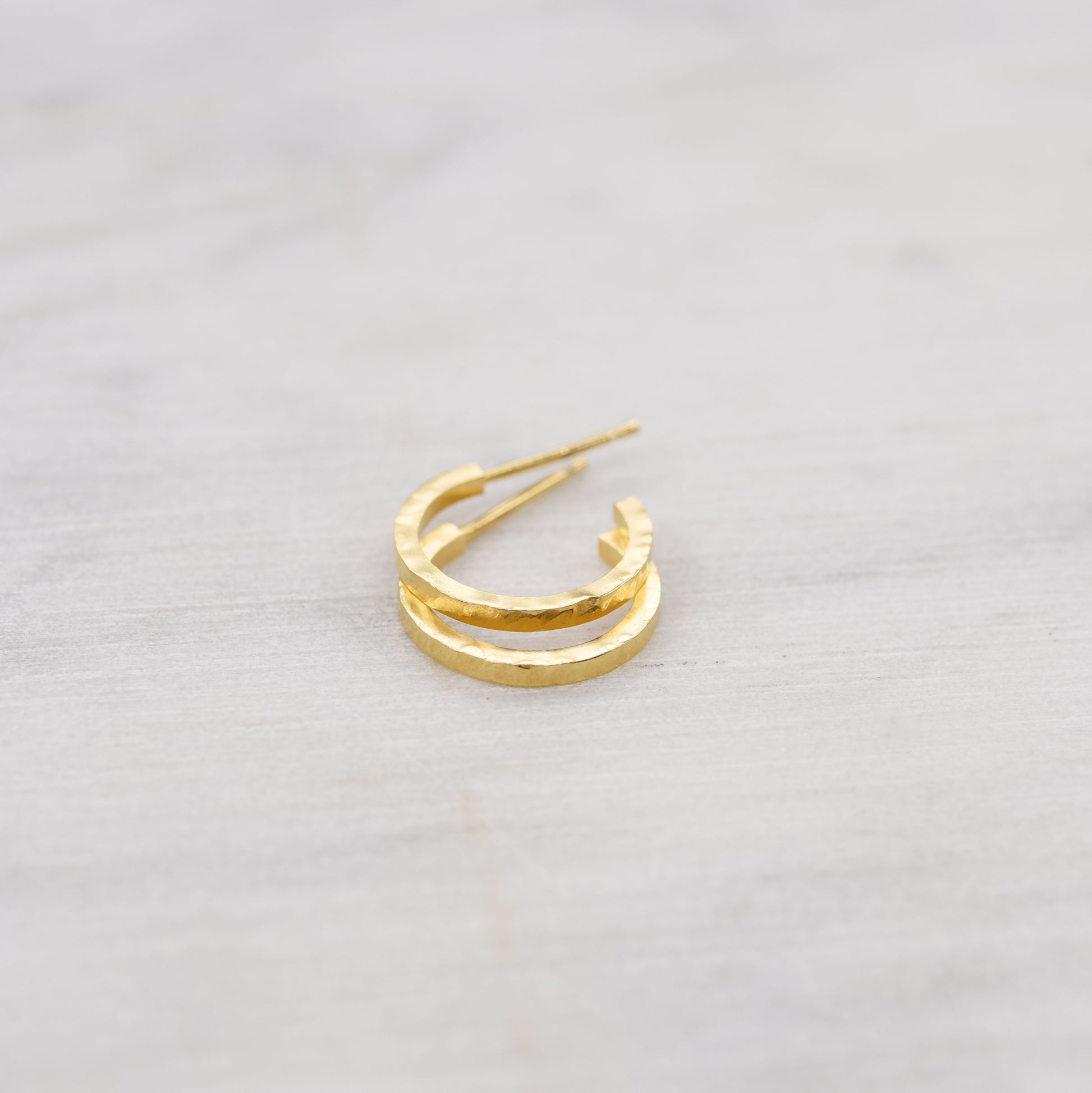 hammered gold hoop earrings on a light marbre background