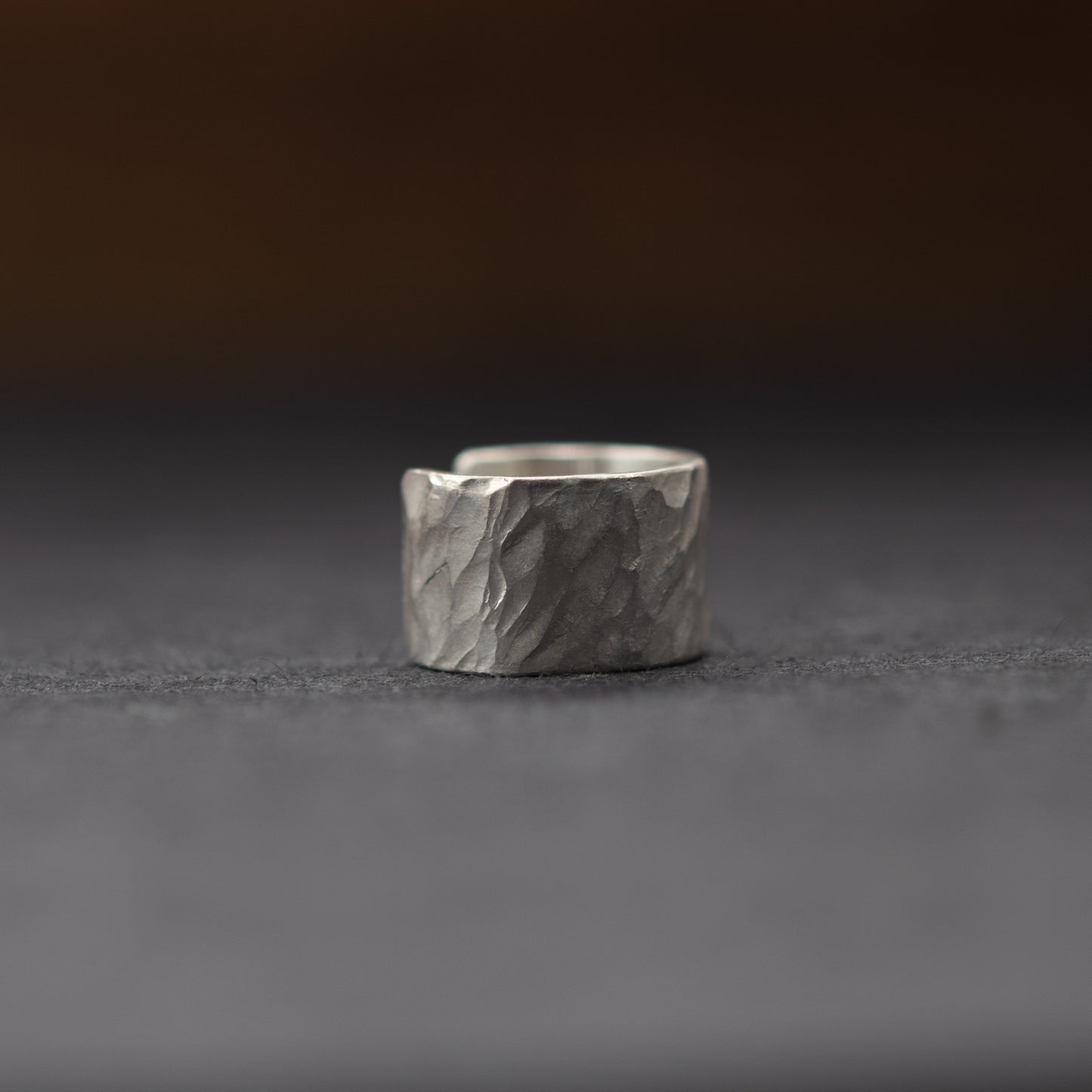 Close-up of hammered sterling silver ear cuff, hand-finished textured surface on dark background
